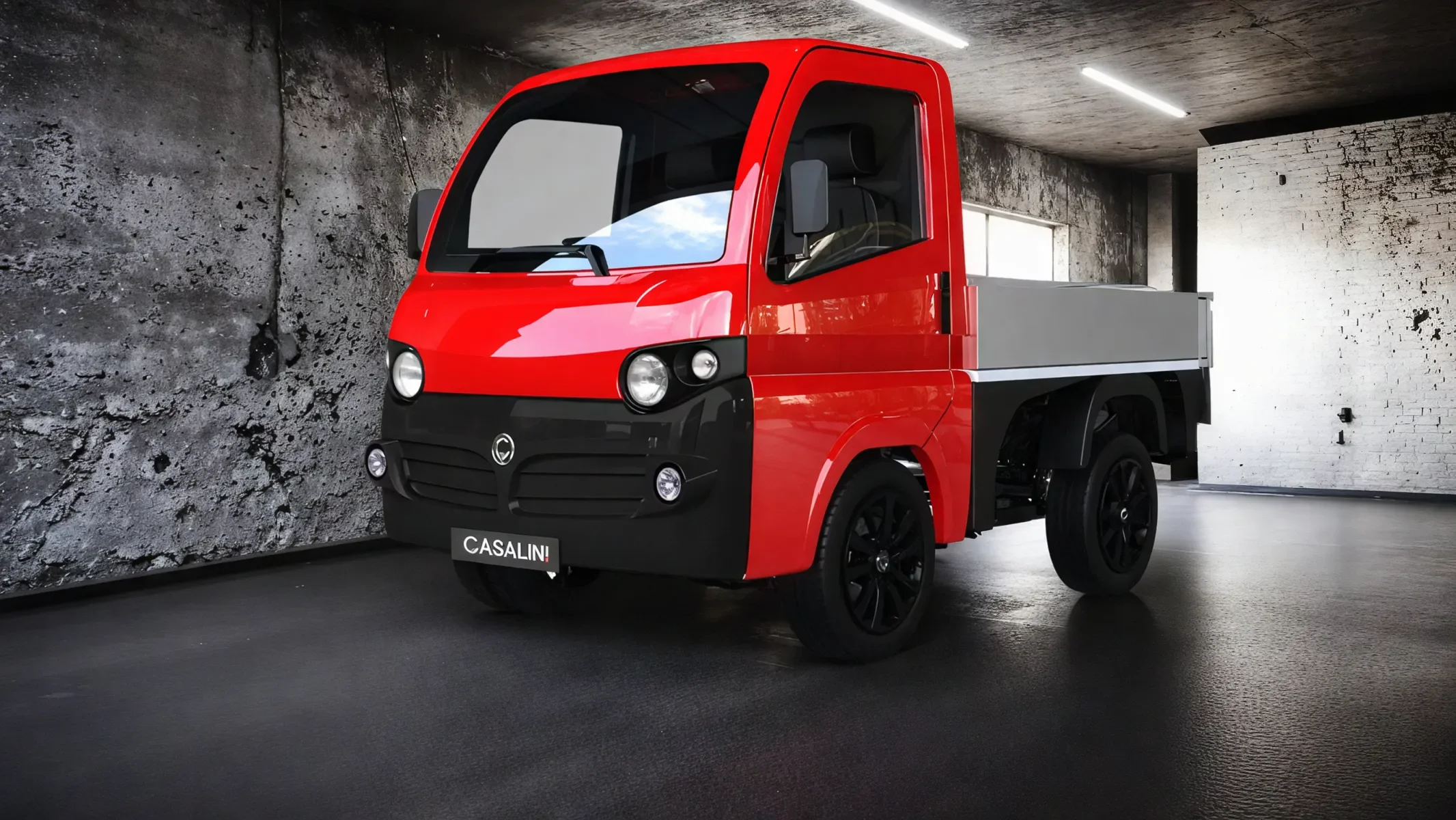 Red and black electric mini truck in a modern industrial showroom with dark floors and concrete walls.