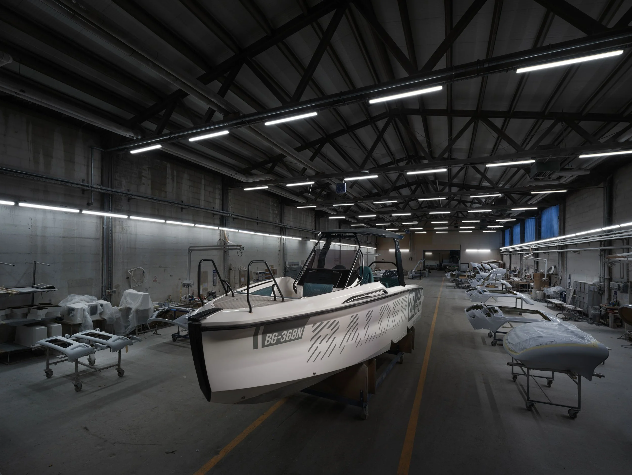 Indoor facility with a boat on a stand, surrounded by other boats and equipment used for boat manufacturing or maintenance.