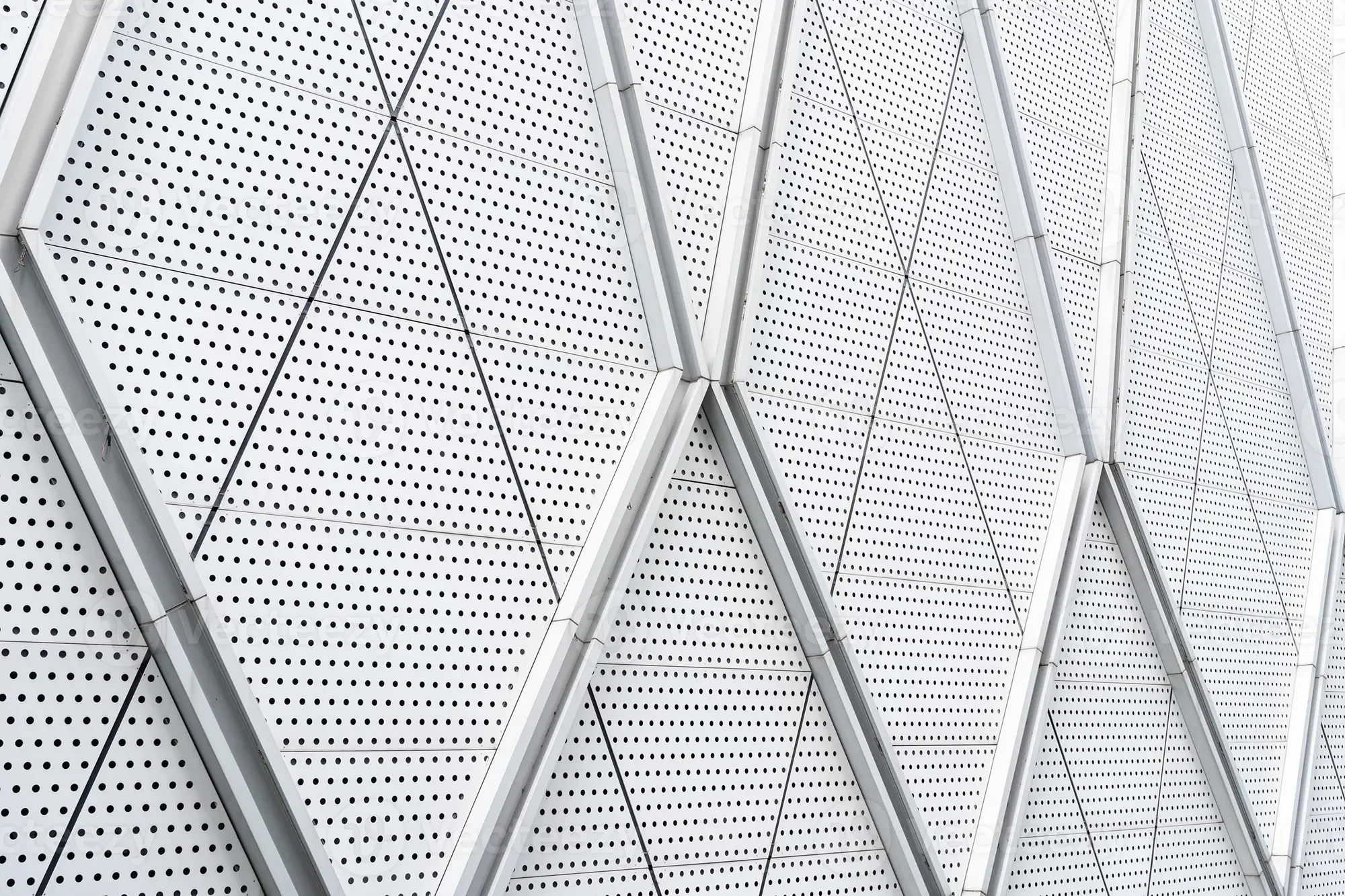 Close-up of a modern building facade with geometric, perforated metal panels and support beams.