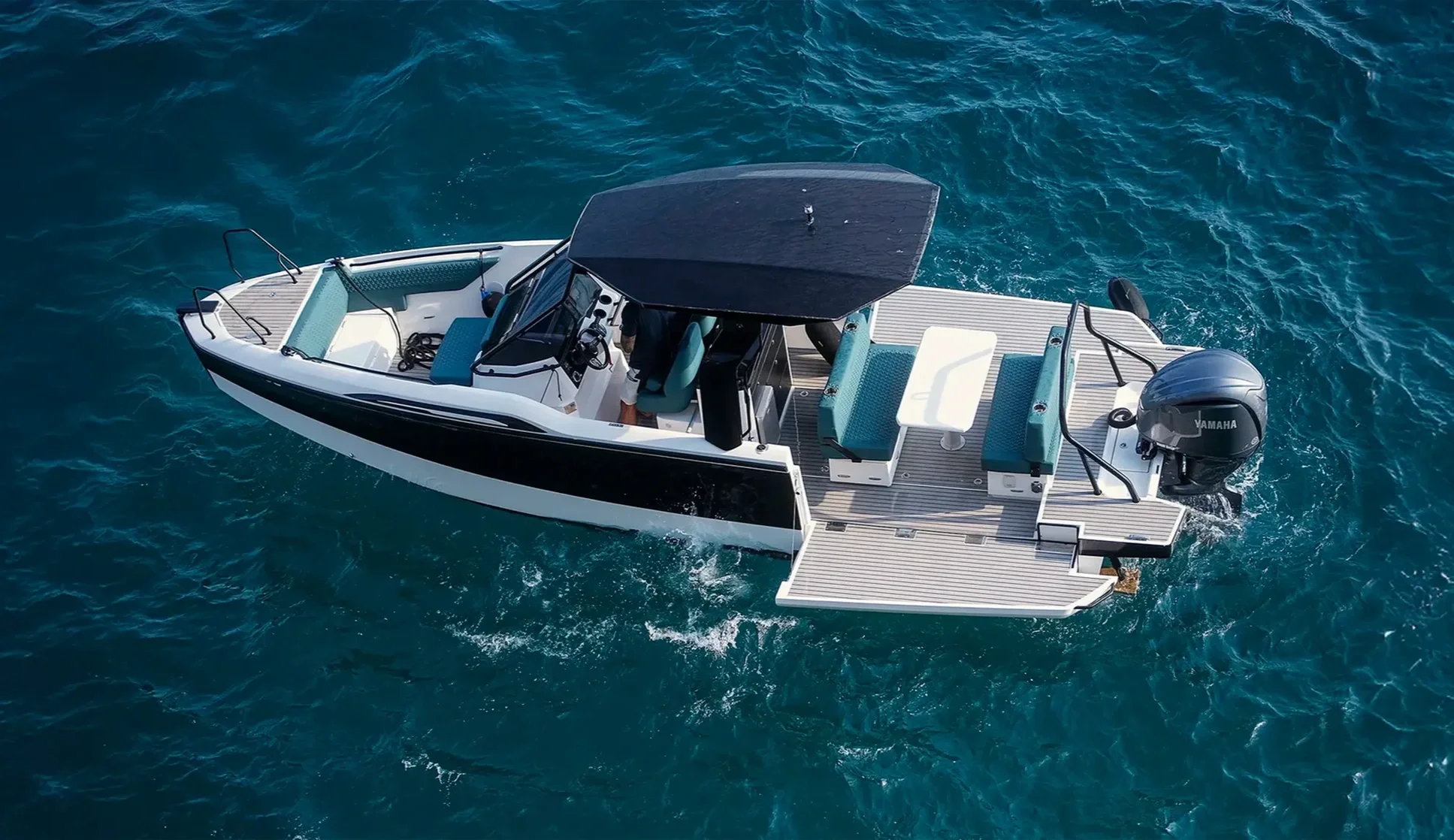 Aerial view of a white and black motorboat with teal seats moving in blue water, featuring a Yamaha outboard engine and a covered steering area.