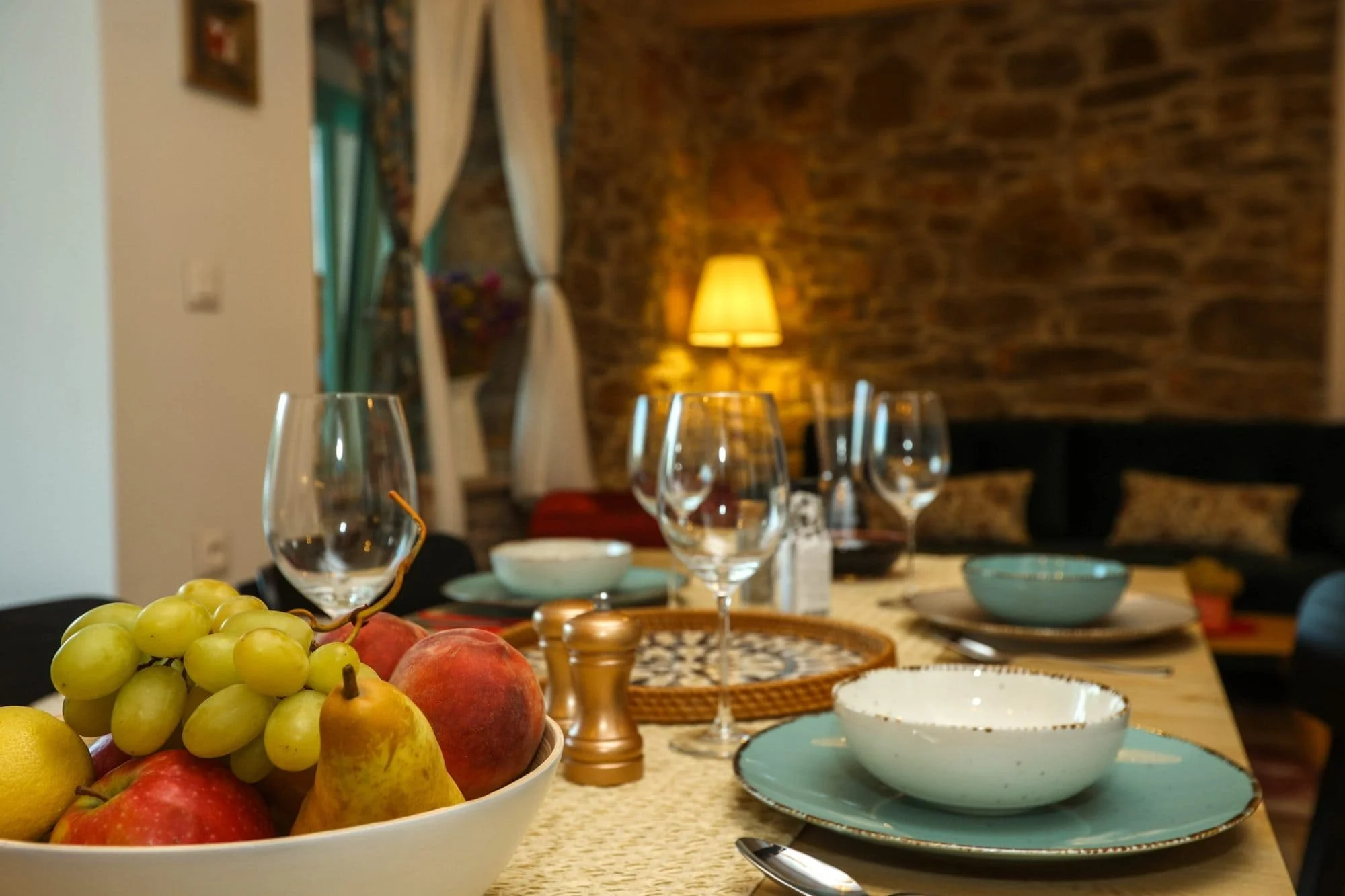 A table set with various bowls, glasses, and fruit, with a brick wall and a lamp in the background.