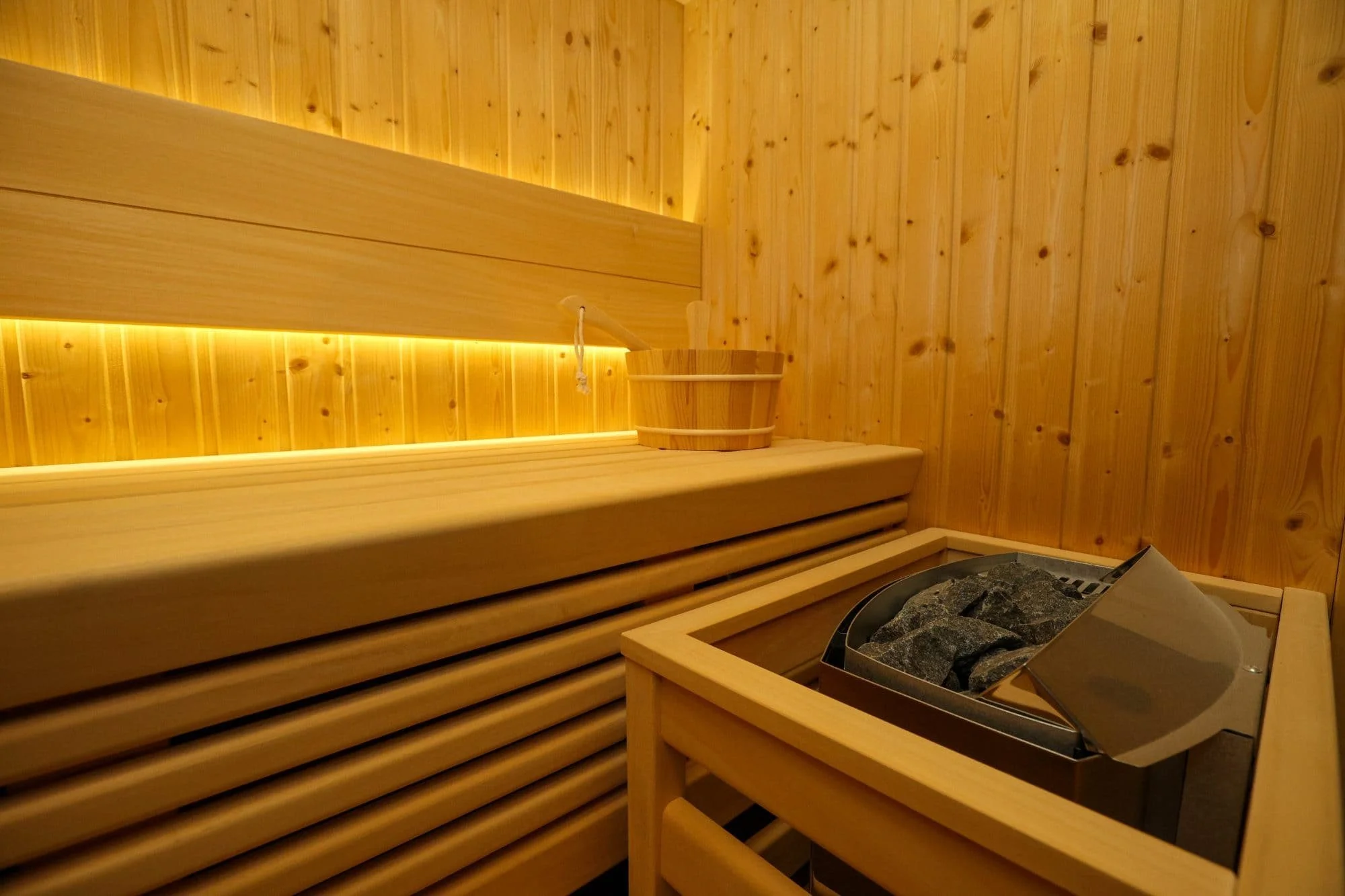 Wood-paneled sauna room with a bench, a bucket, and a heater with rocks.