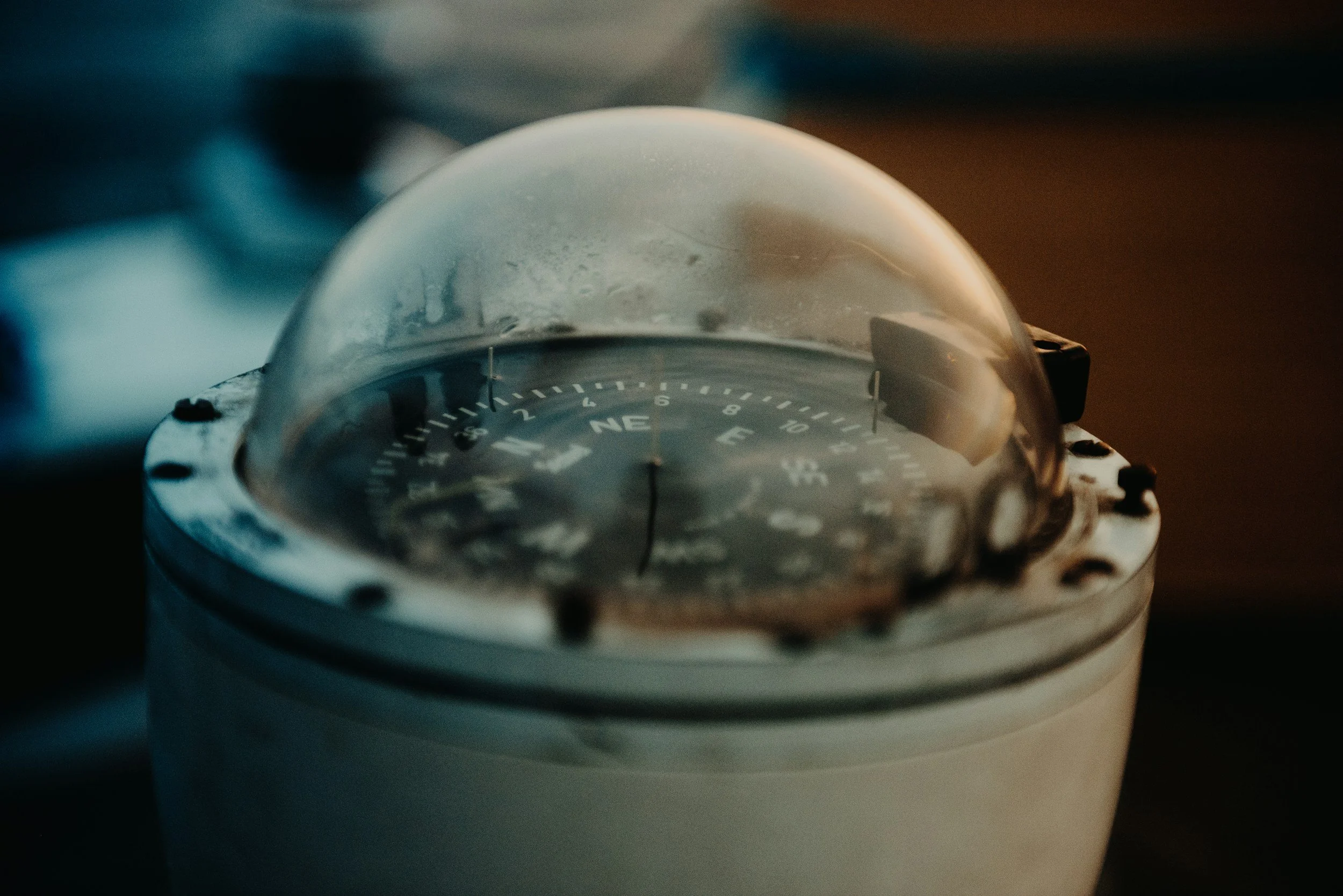 Close-up of a marine navigation compass with a transparent dome, showing directions and latitude markings, mounted on a gray base.