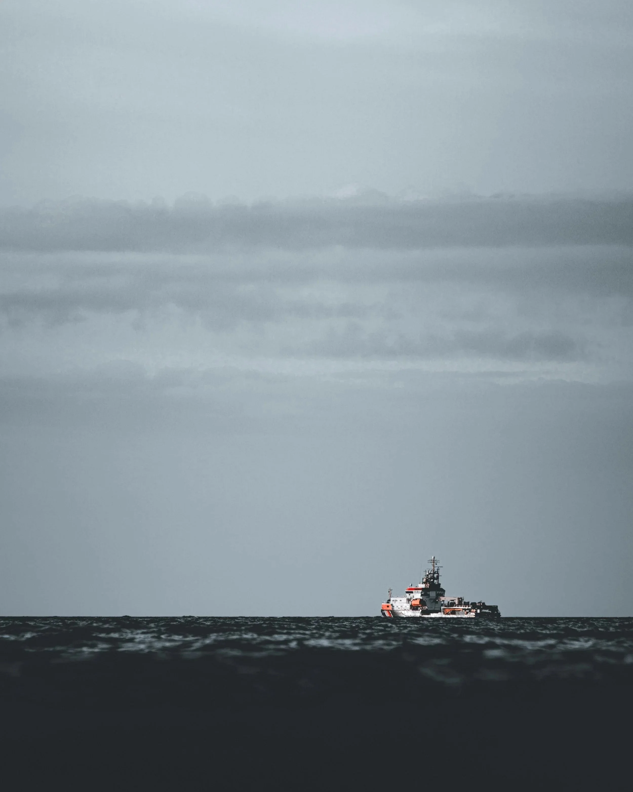 A ship floating in dark water beneath a cloudy sky.