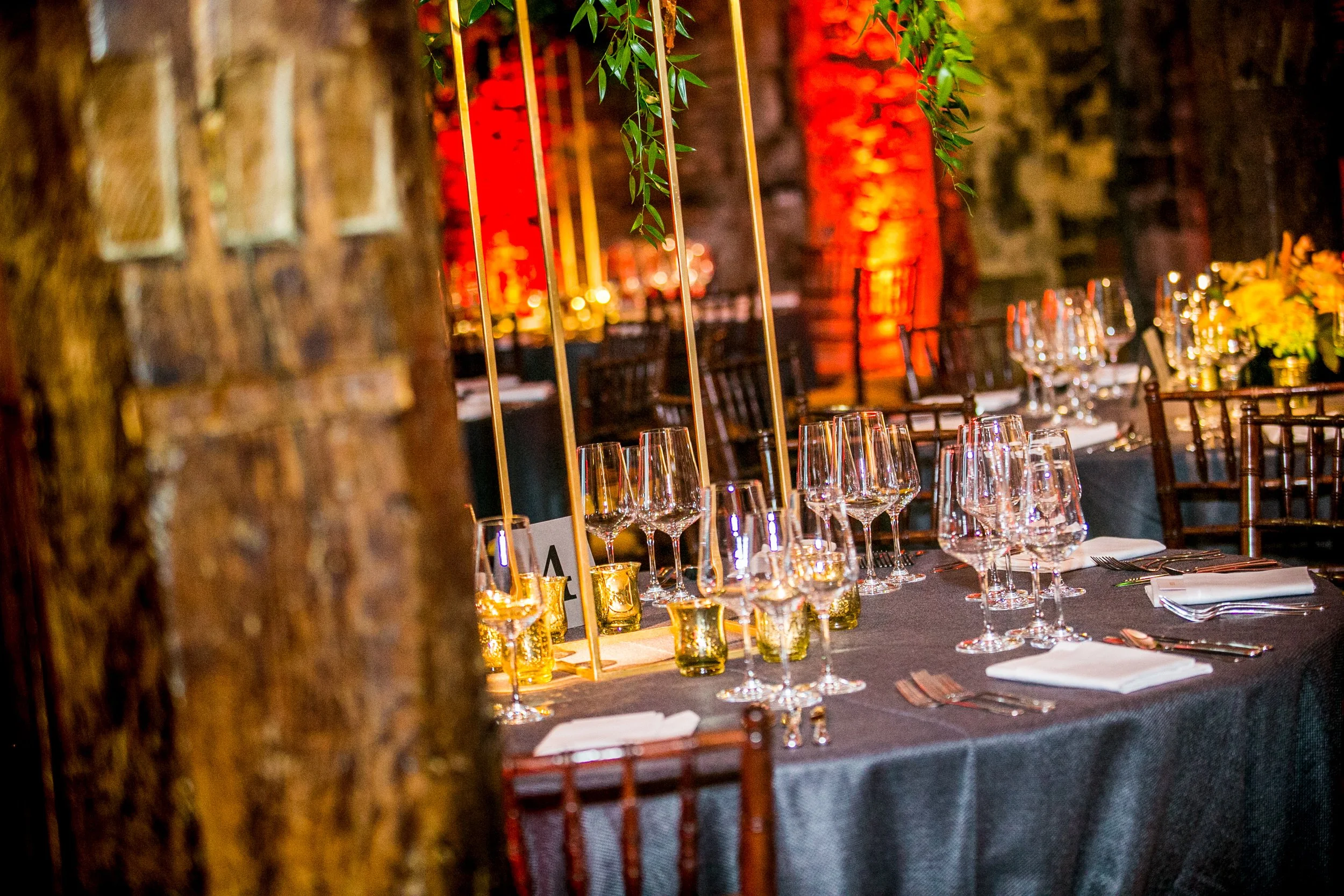 A beautifully set dining table with wine glasses, candles, and elegant floral arrangements in a warm, ambient lighting setting, decorated with greenery and dark table linens at the Tower of London