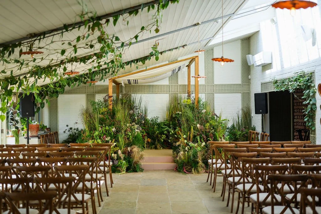 Chupppah set up at Kin Houe ready for the wedding ceremony space with wooden chairs, lush greenery, and a decorated altar on a small stage.