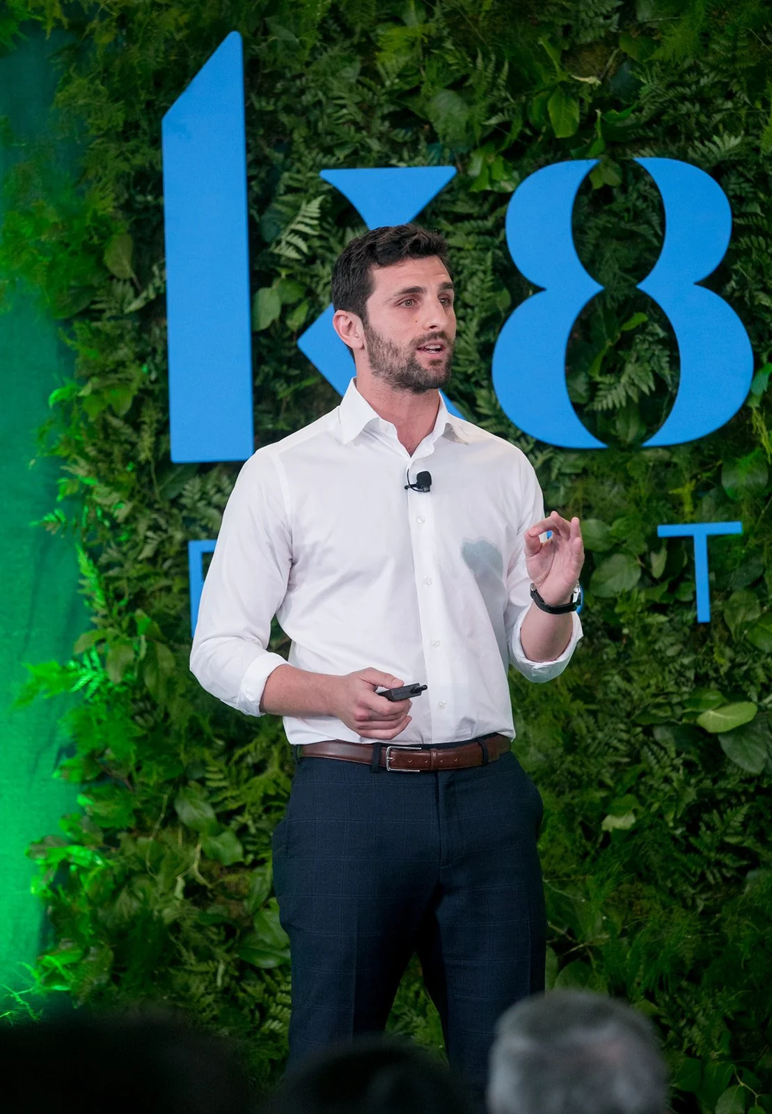 A man in a white shirt giving a presentation in front of a green leafy backdrop at a conference 