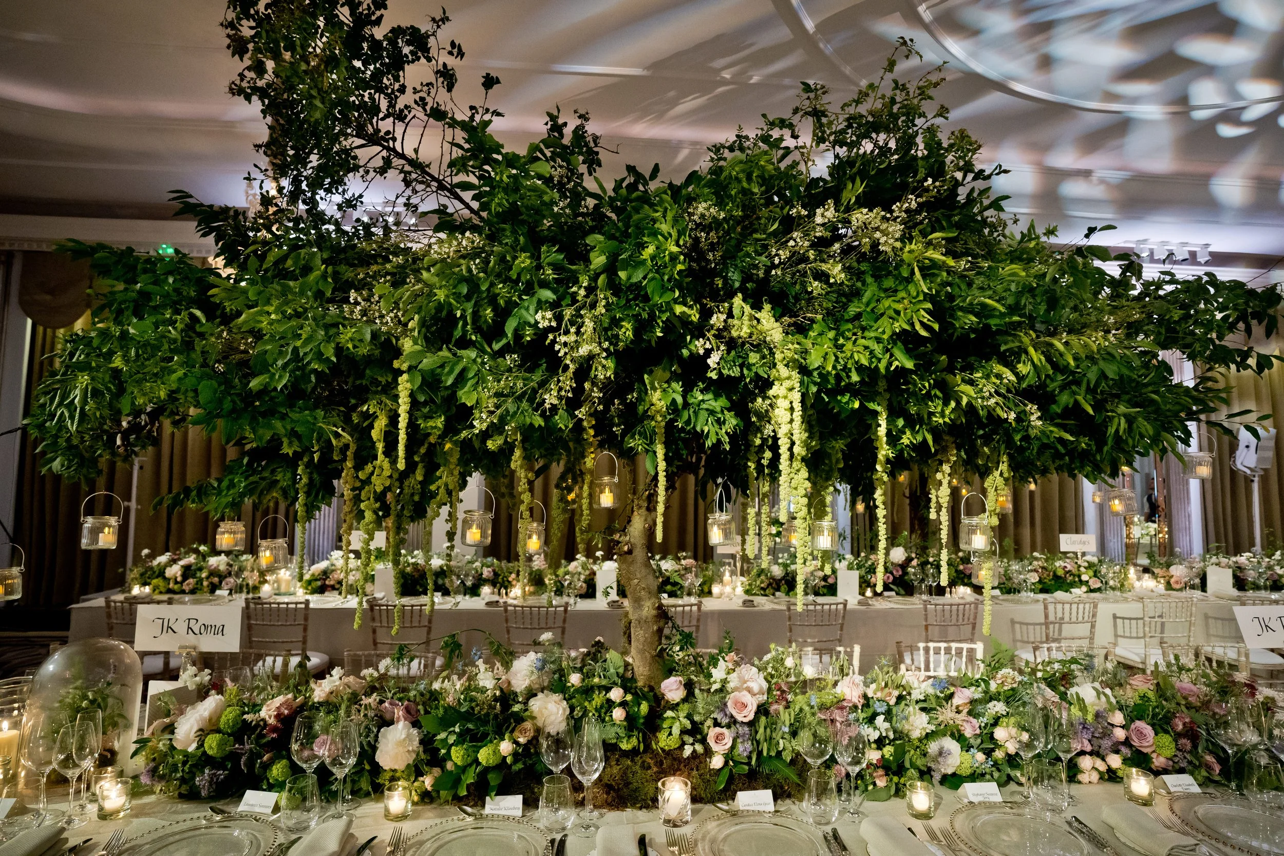 Decorative indoor wedding reception with a large hanging floral arrangement surrounded by candles and floral centerpieces at the tables.