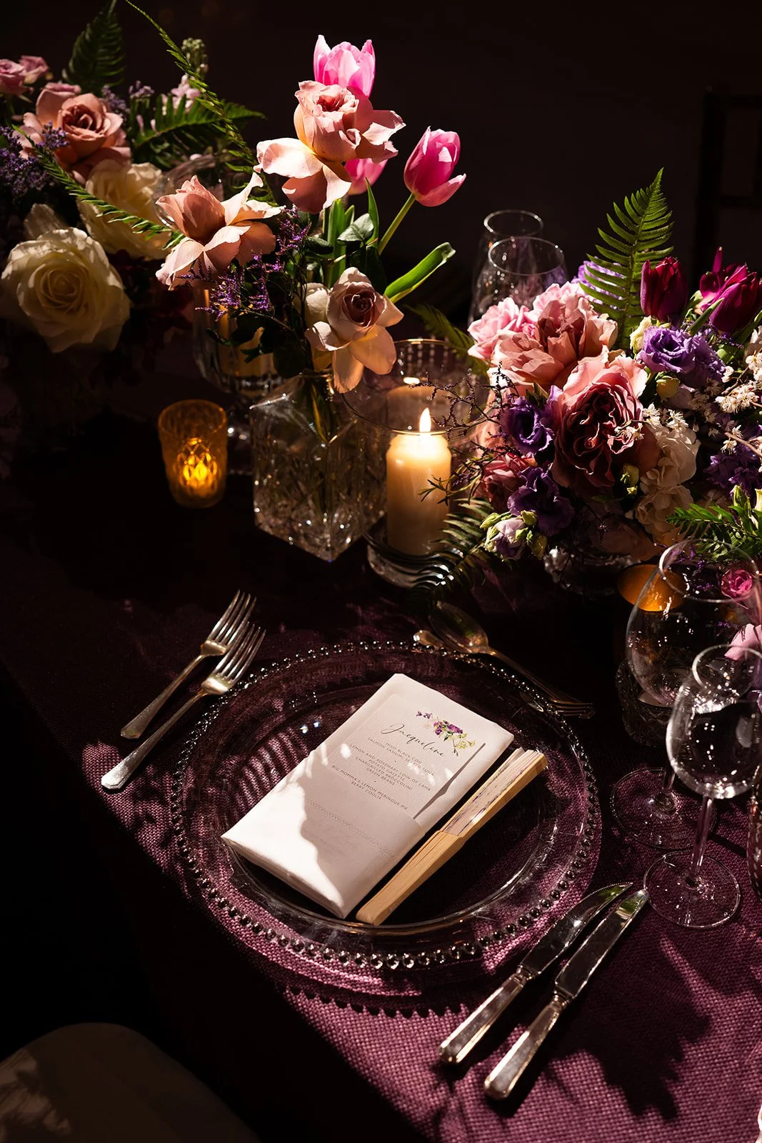 Elegant table setting with floral centerpiece, lit candle, glassware, and a place card on a purple tablecloth at The Peninsula London