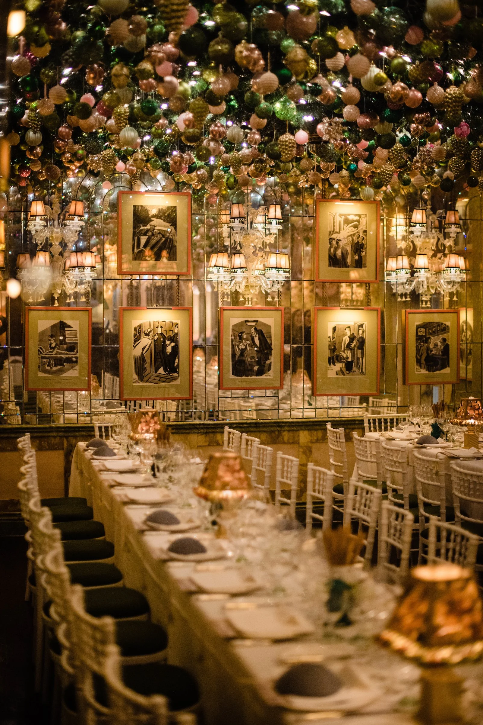 Elegant restaurant interior with long dining table set with white tablecloths, glassware, and napkins, and decorated with warm lighting and wall art.