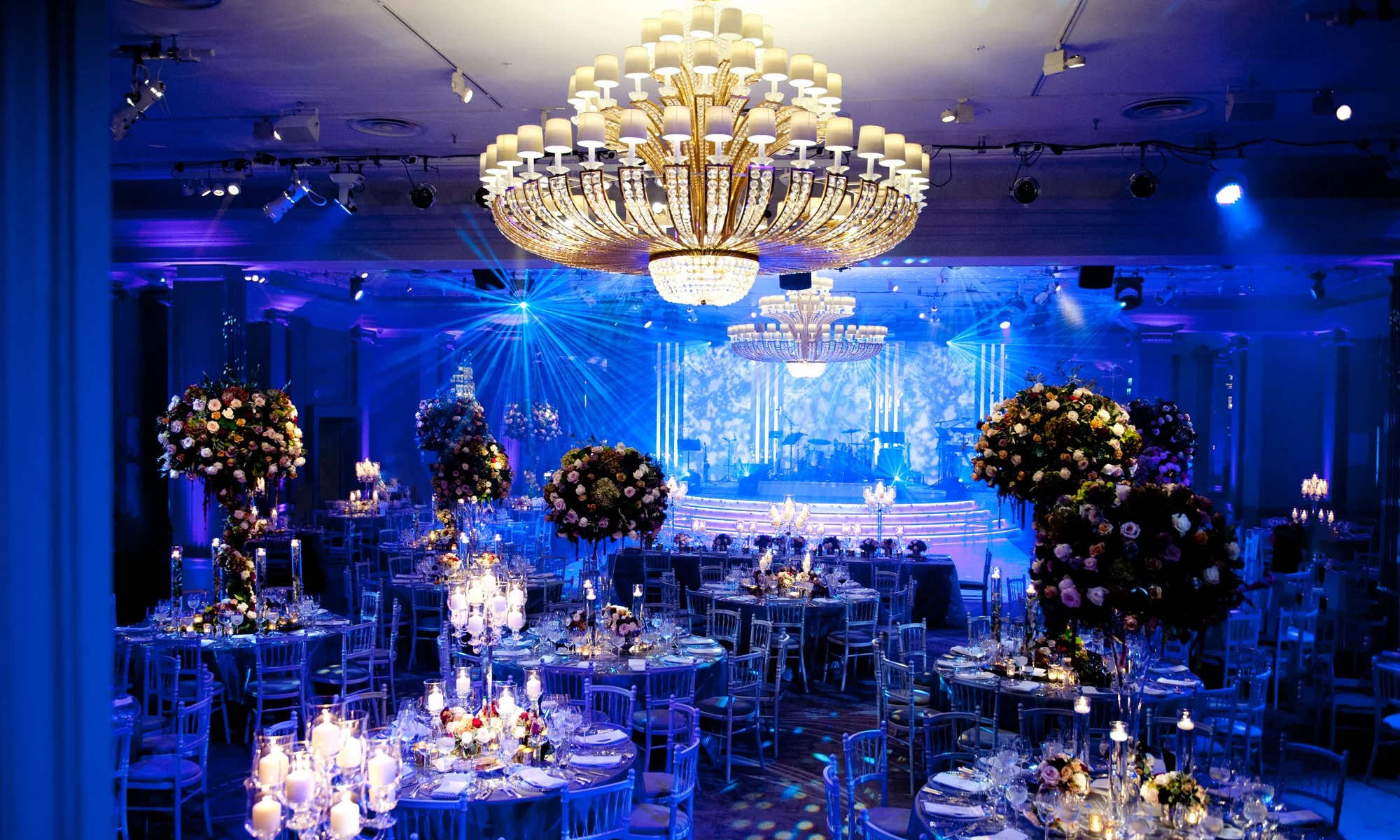 Elegant event hall decorated with grand chandeliers, floral centerpieces, and blue lighting for a formal wedding at Grosvenor House.