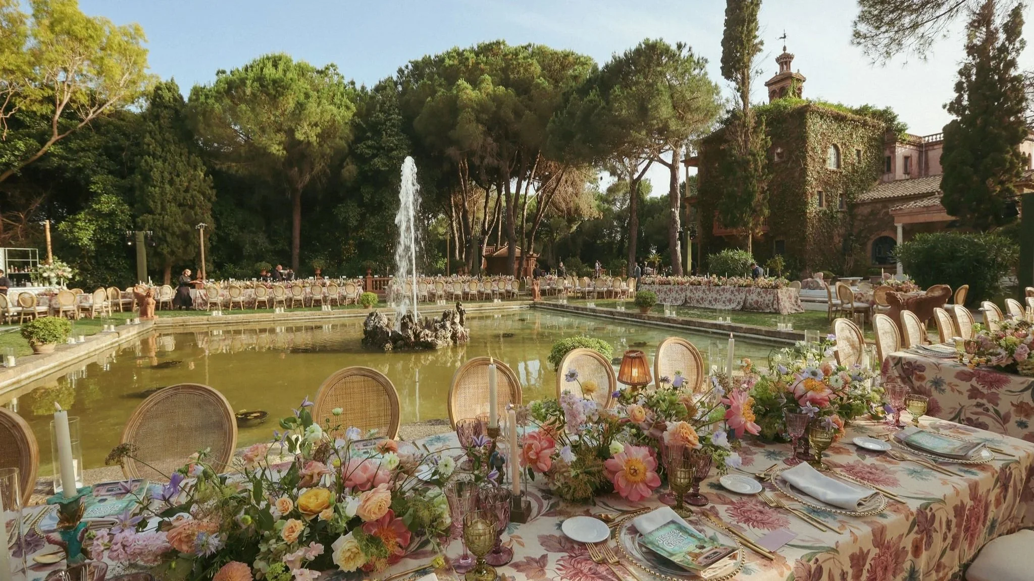 Spanish wedding with outdoor dining setup next to a fountain with surrounding trees, tables with floral tablecloths, and pink and purple floral centerpiecesat the Anantara Villa Padierna Resort in Marbella