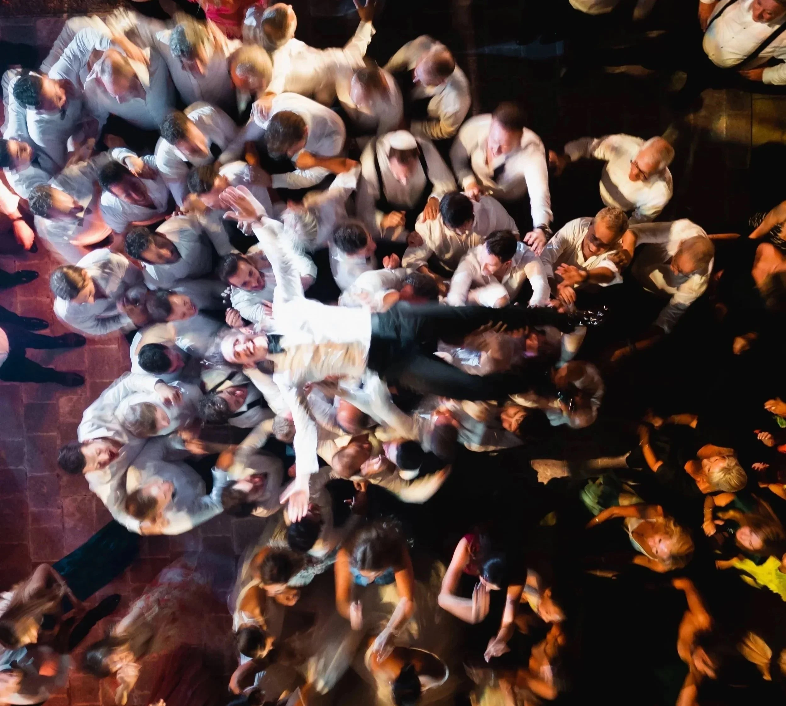 Crowd of people dancing and celebrating at a party or event, dressed in white and colorful outfits, with smiles and energetic movements.