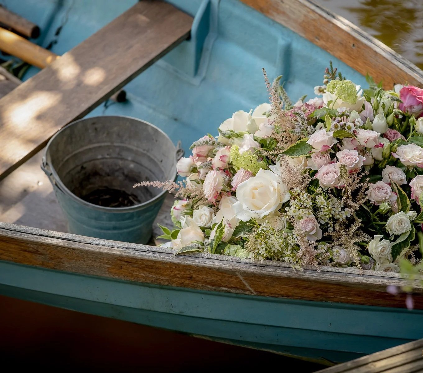A bouquet of white and pink roses with greenery in a wooden rowboat on water