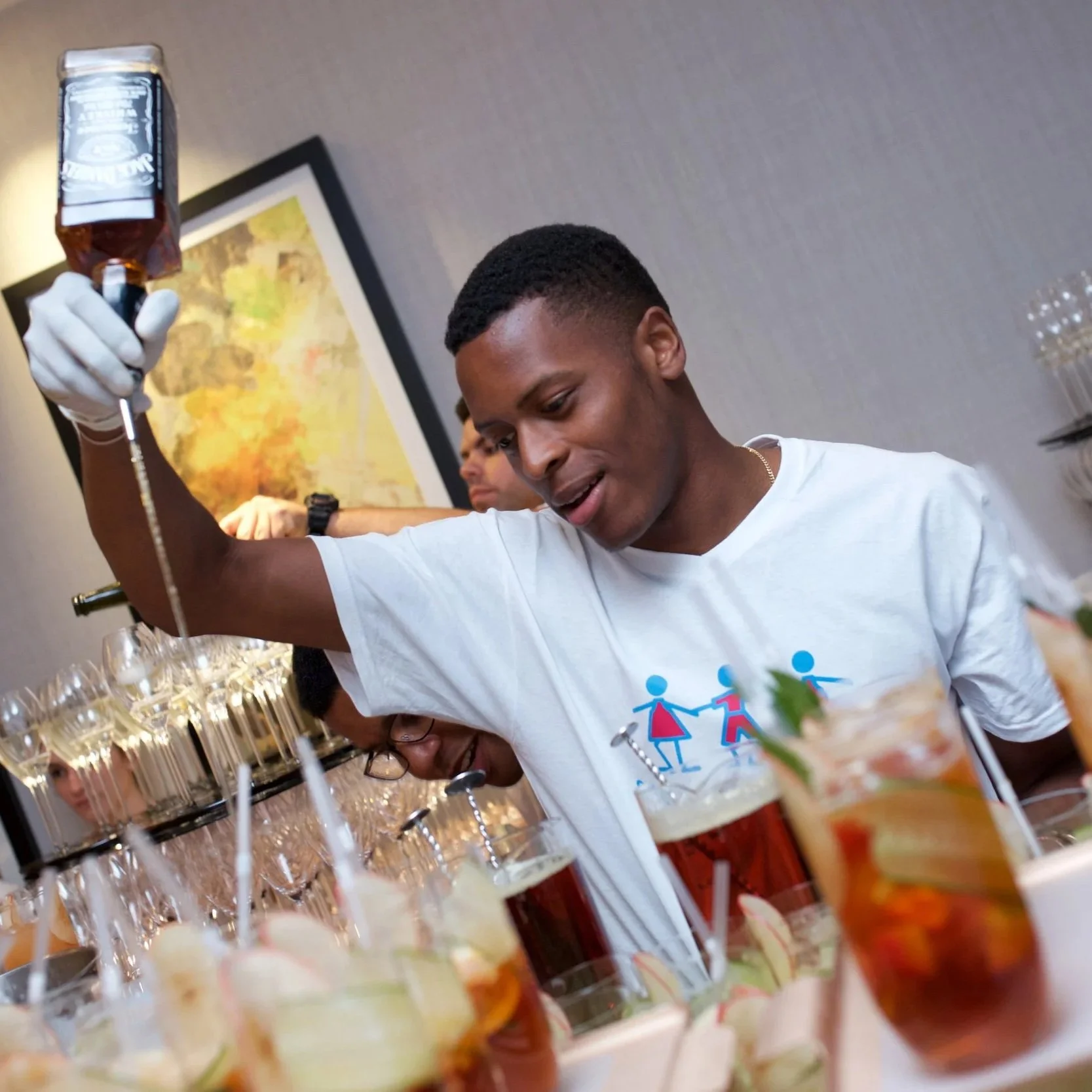 Group of people at a party or gathering, smiling and enjoying drinks near a bar with alcoholic beverages, glasses, and drinks with garnishes on the table.