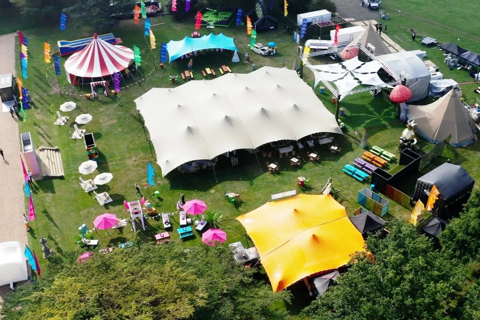 Colorful outdoor event setup with tents, picnic tables, umbrellas, and seating areas on a grassy field for a Bar Mitzvah at  Wrotham Park