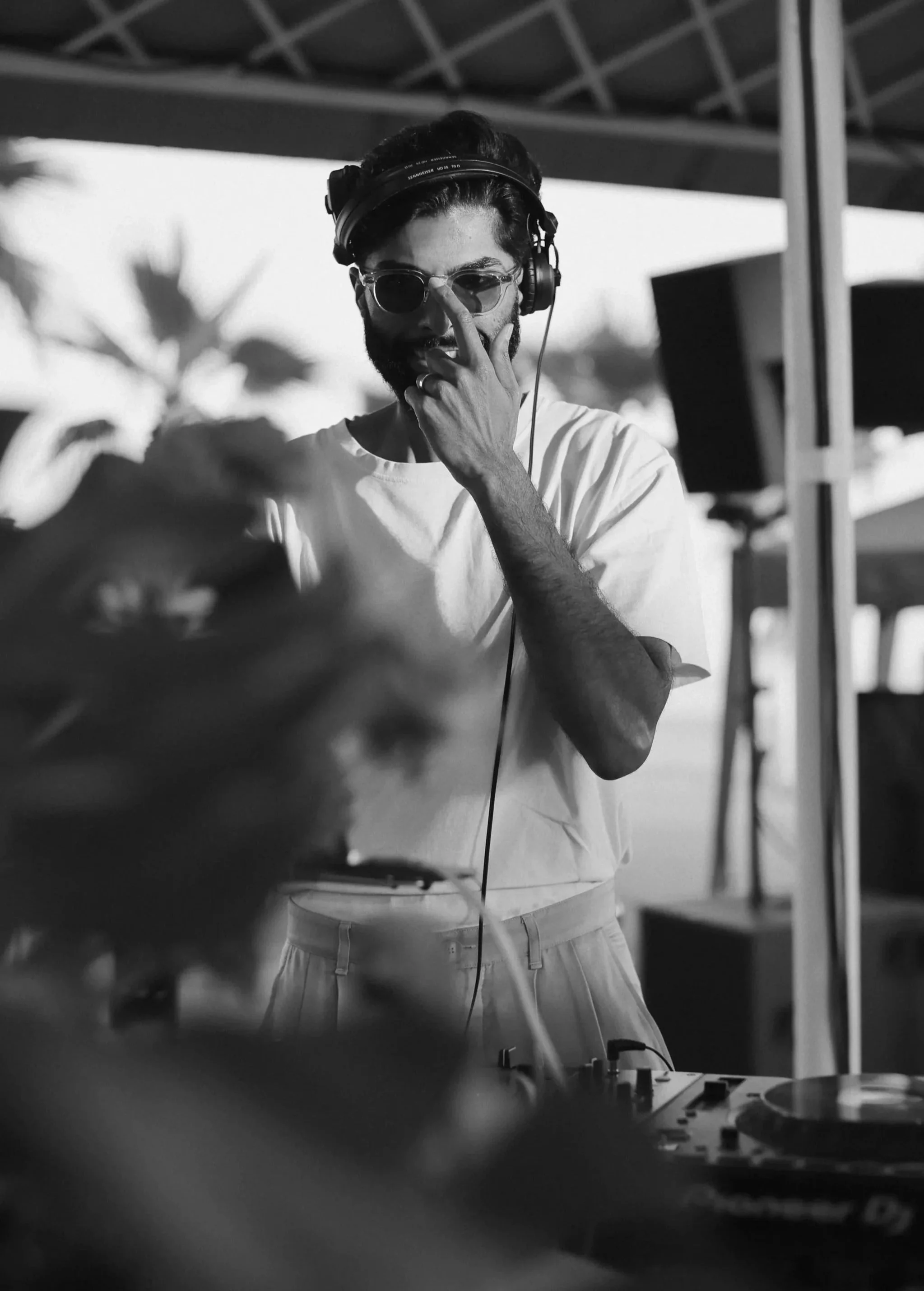 Black and white photo of a man with a beard wearing sunglasses, headphones, and a white t-shirt, adjusting his sunglasses while working with DJ equipment outdoors at Anantara Villa Padierna Resort in Marbella
