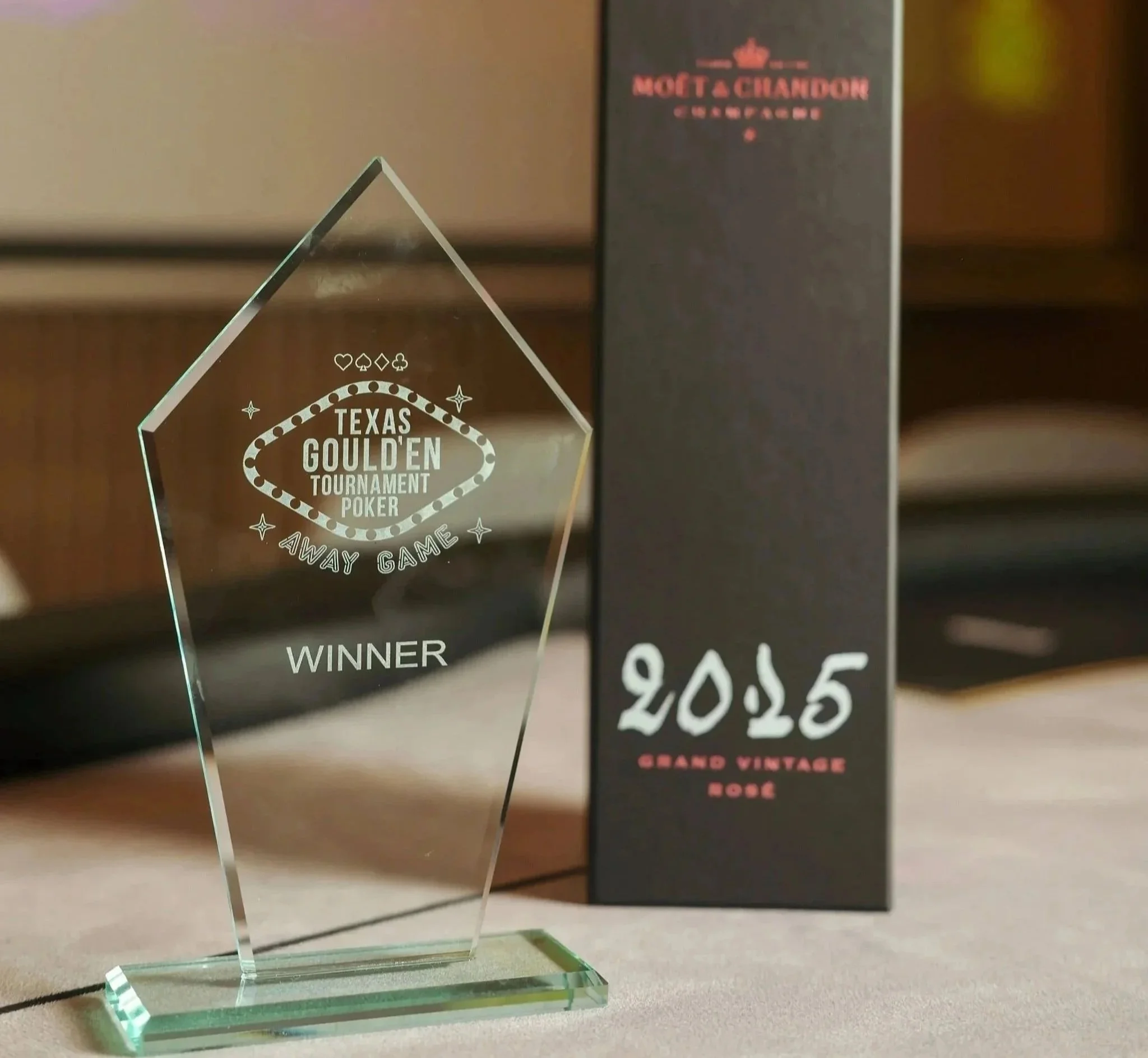 A clear glass trophy shaped like a diamond with the words 'Texas Goulden Tournament Poker' engraved on it. Moët & Chandon Champagne' and some prices listed on a chalkboard at Anantara Villa Padierna Resort in Marbella