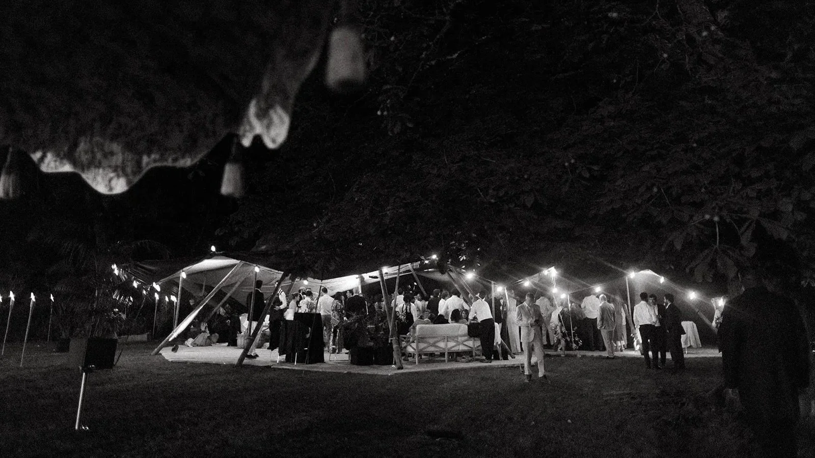 The afterparty for private residents hertfordshire wedding  under a large tent with string lights, featuring people socializing and standing around tables.