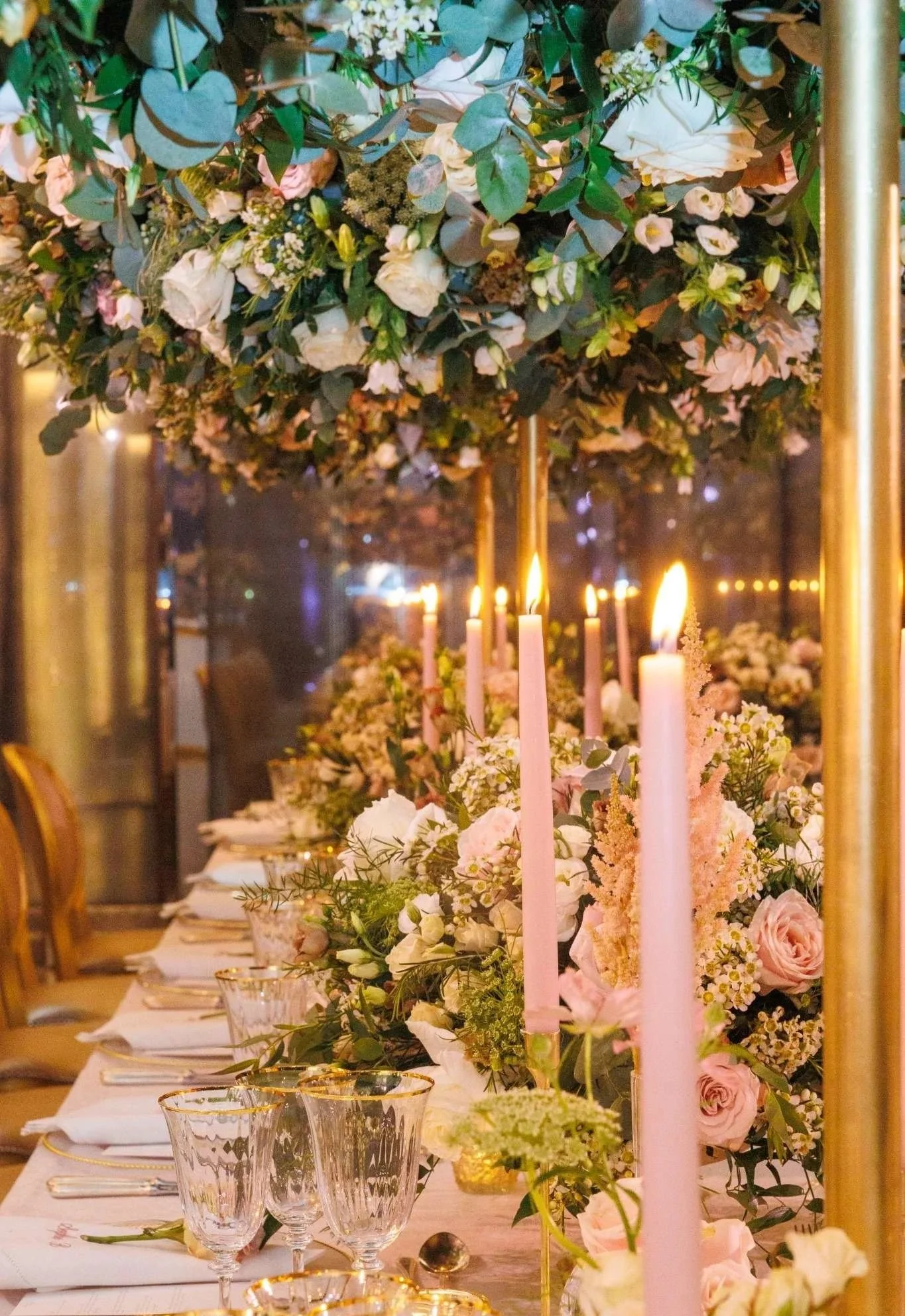Elegant banquet table decorated with a large floral centerpiece, pink candles, glassware, and table settings in a warmly lit venue.