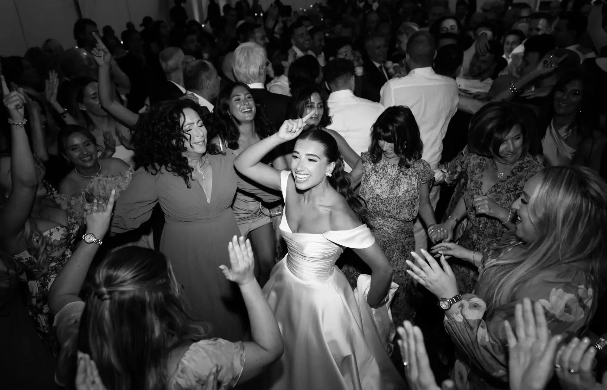 A group of people dancing and enjoying themselves at a lively party or celebration, with a woman in a strapless dress smiling and dancing in the center.