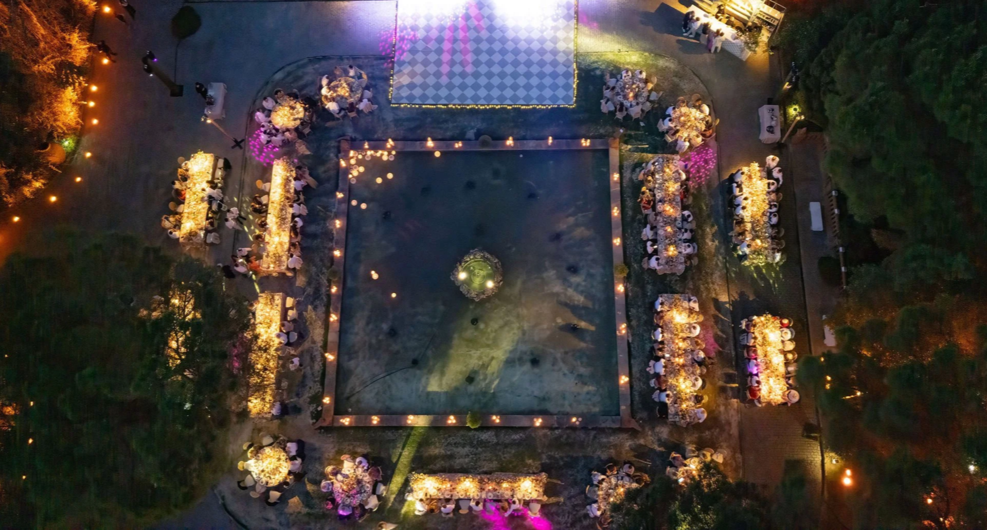 An aerial view of an outdoor event at night with tables decorated with flowers and candles, set up around a central dance floor, illuminated with colorful lights of Anantara Villa Padierna Resort in Marbella