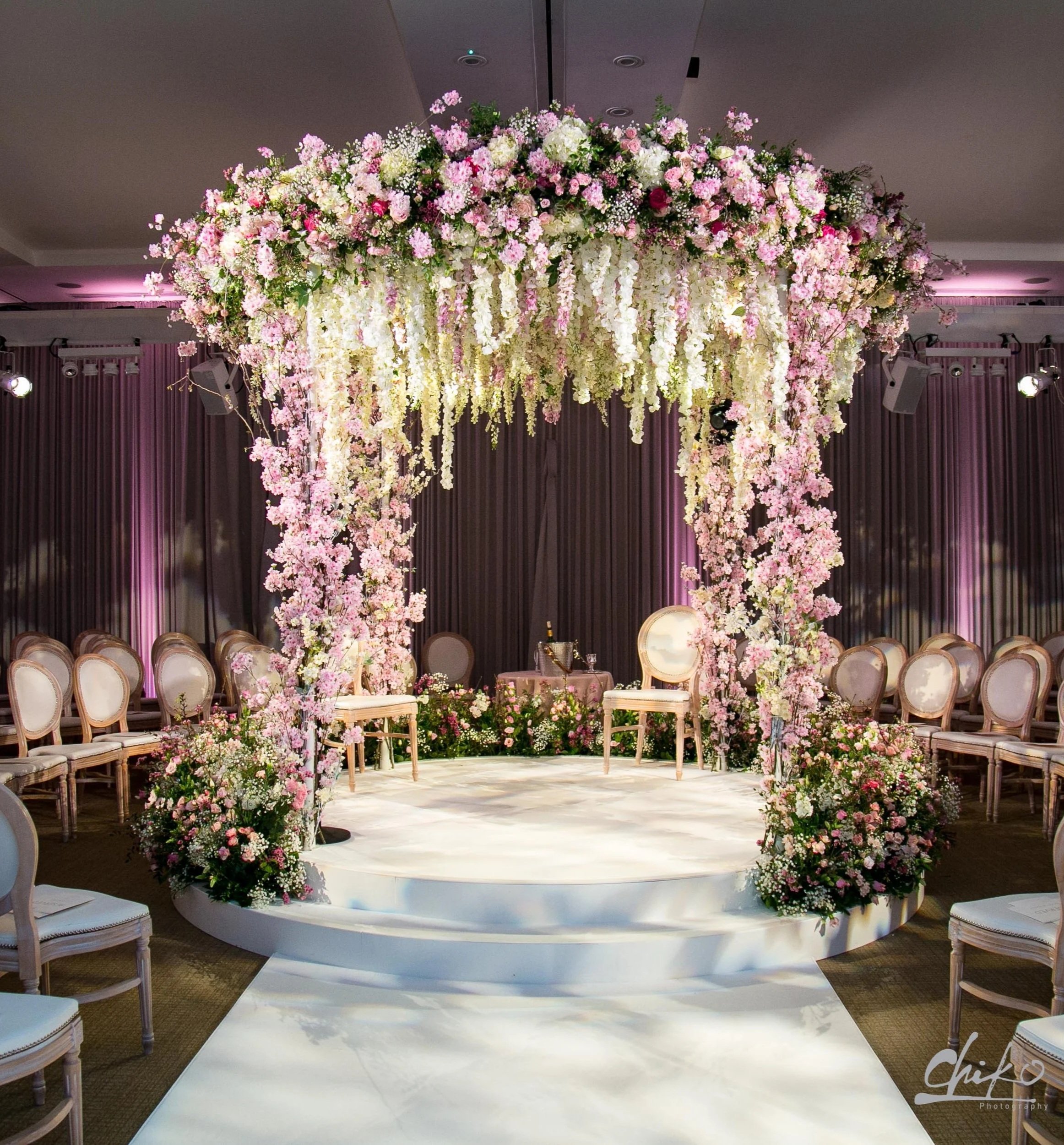 Elegant wedding ceremony setup with a floral arch and chairs arranged in a semi-circle on a white platform at Rosewood London