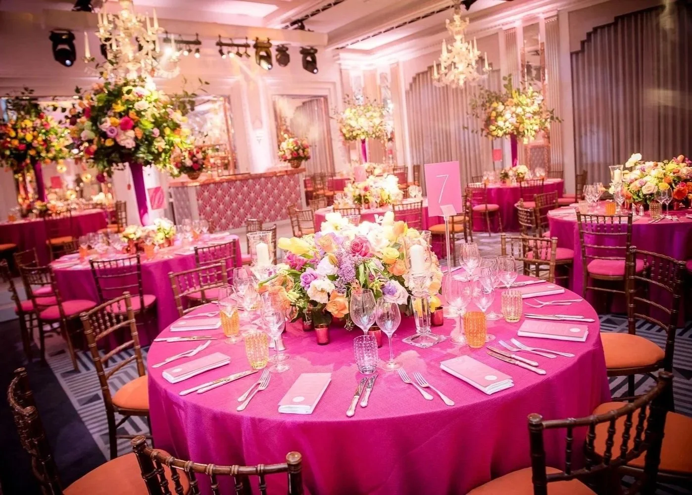 Elegant banquet hall decorated with pink tablecloths, floral centerpieces, and chandeliers, set for a wedding or special event.