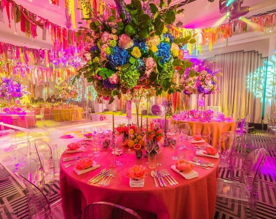 Decorated Claridge's hall with pink tablecloths, floral centerpieces, and colorful garlands and lighting.