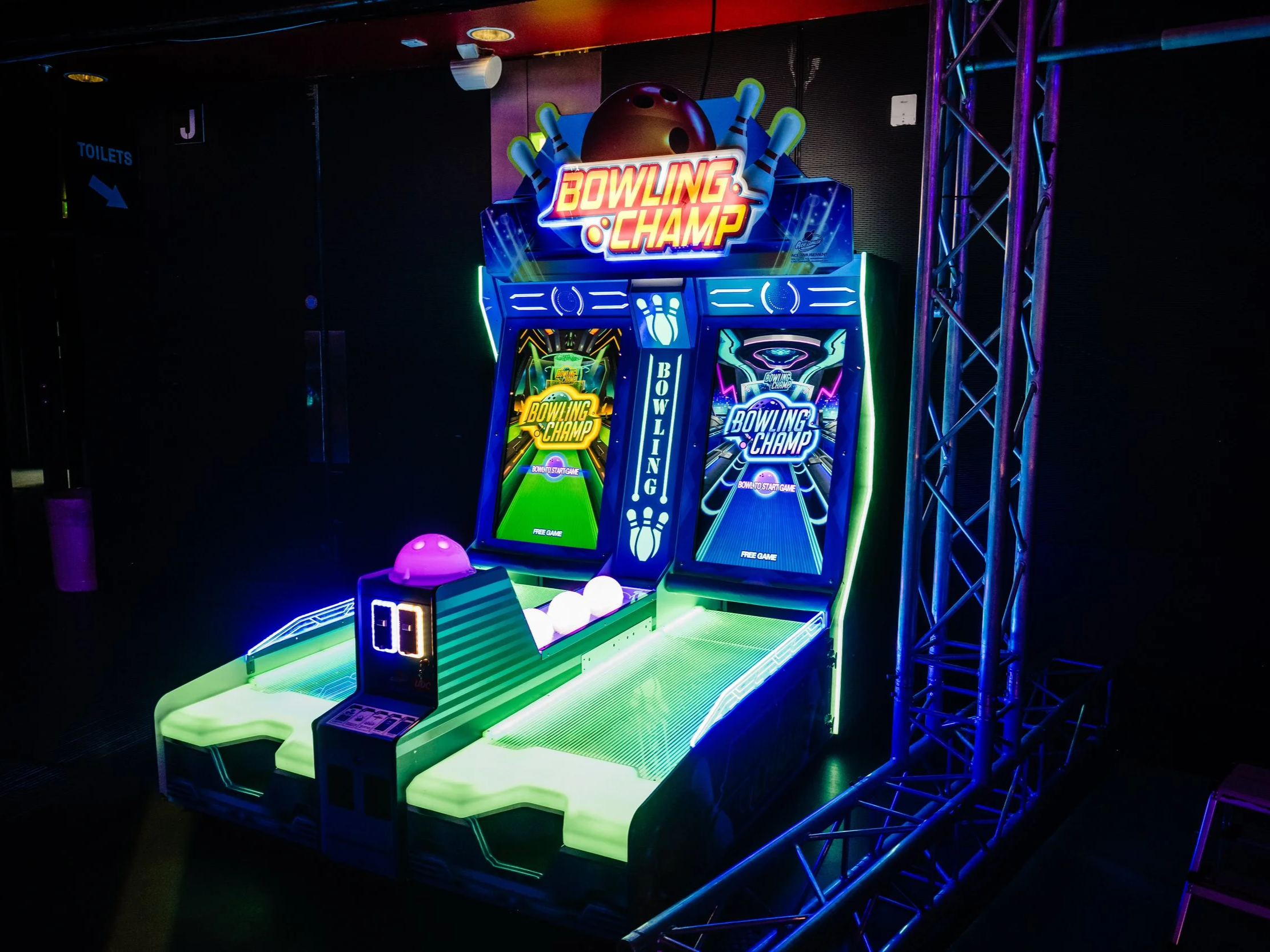 Colorful arcade bowling game with neon lights, screens displaying game instructions, and a bowling ball at the start area in a dark entertainment venue.