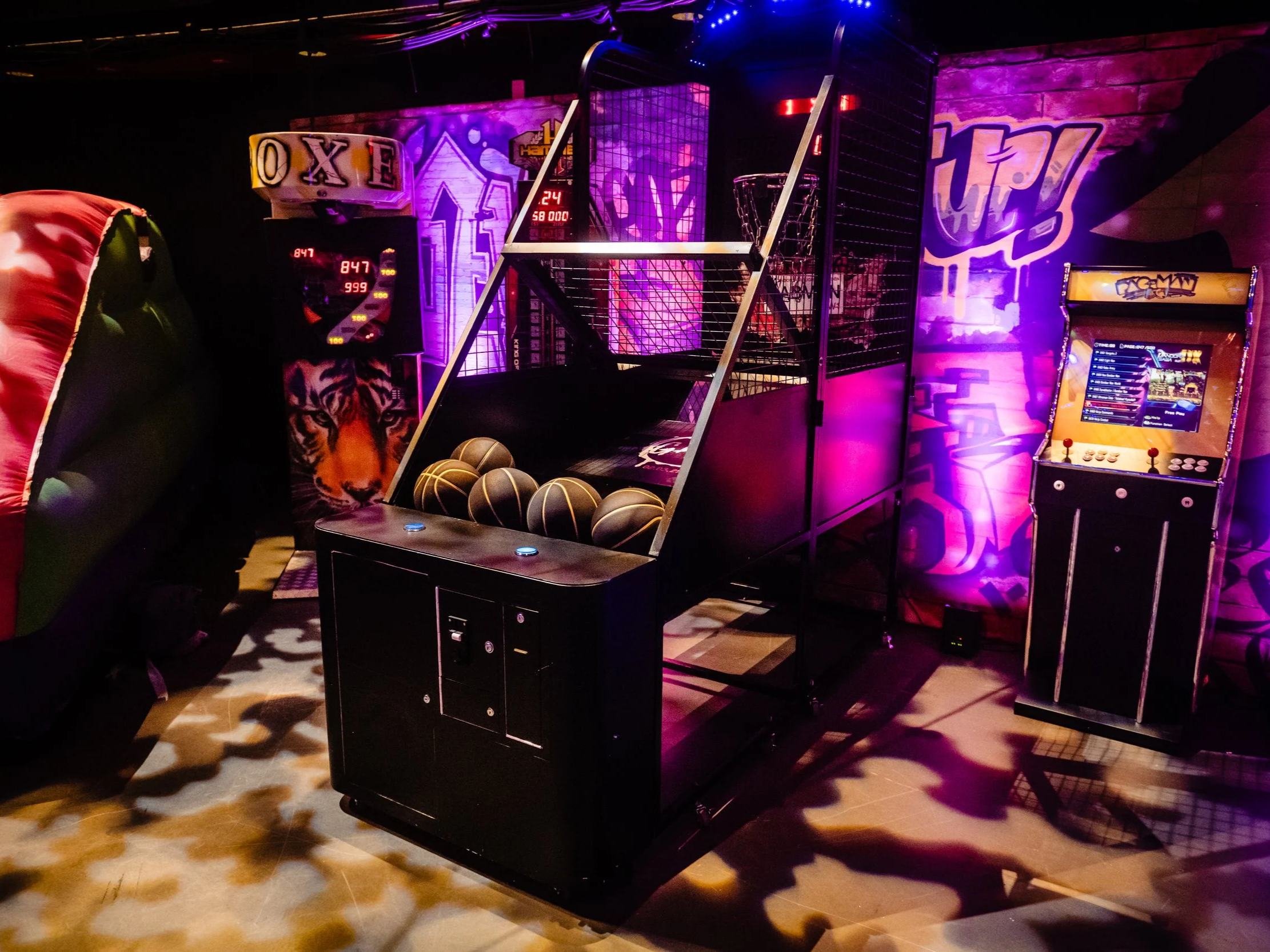 Indoor arcade with basketball game, arcade machine, and neon purple lighting, casting shadows on the floor at a Bar Mitzvah 
