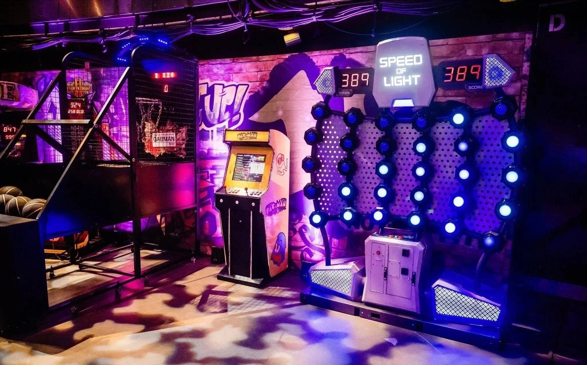 A Neon Lights arcade game with digital score displays, surrounded by purple and blue lighting, situated in an arcade with graffiti art on the brick wall in the background at the Roundhouse London