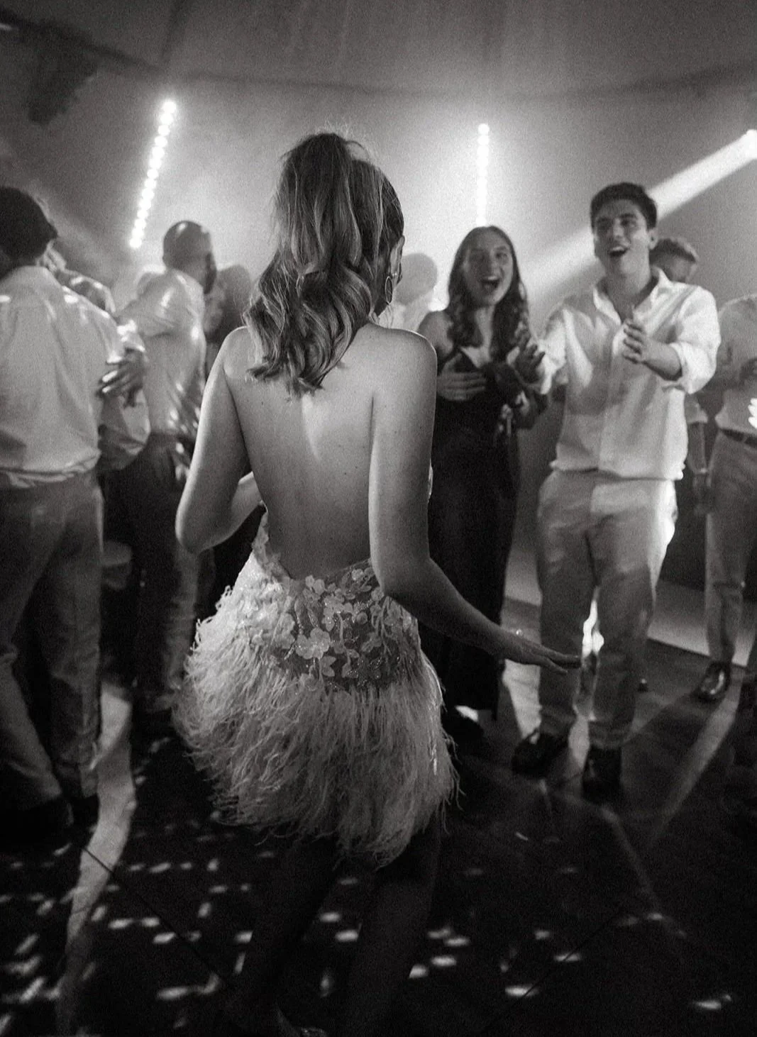 People dancing at the wedding afterparty, with a woman in a detailed costume dancing in the foreground, surrounded by others smiling and enjoying the event in a dimly lit room.