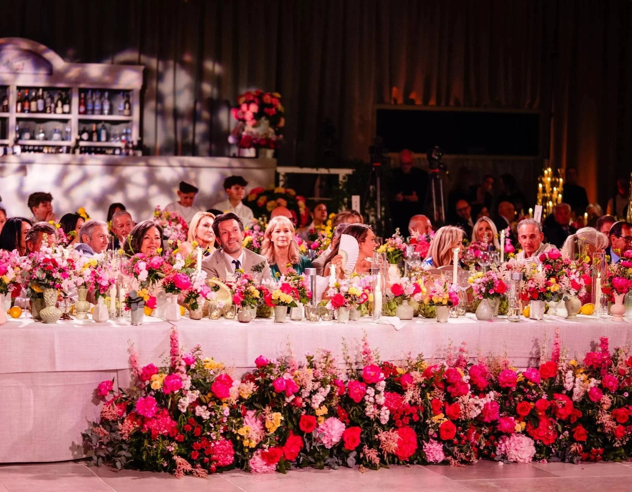 Crowd of people seated at a long table decorated with pink and red flowers at a formal event Fairmont Windsor Park'.