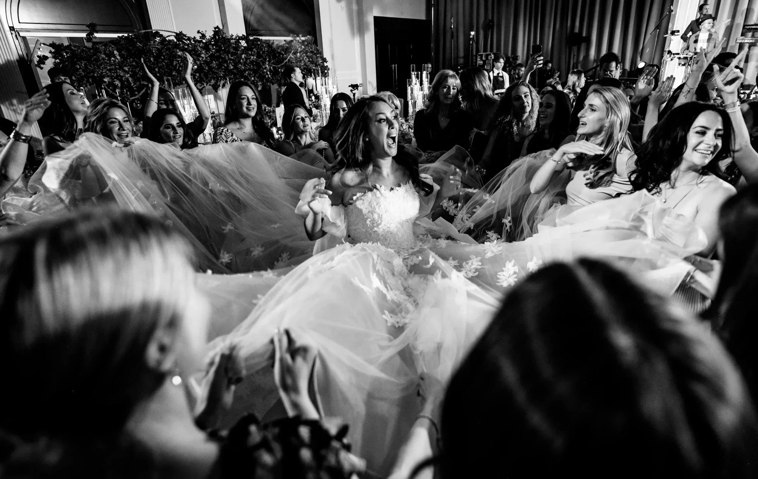 A group of women at a celebration or party, some wearing dresses and smiling, with one woman in the center wearing a white dress and a tulle skirt, appearing excited and joyful Fairmont Windsor Park