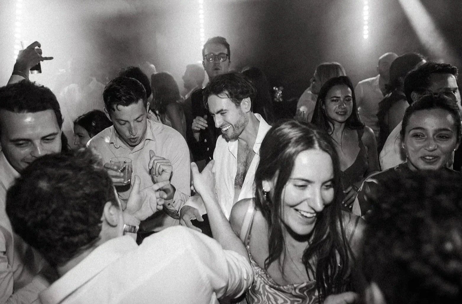 A group of people dancing and socializing at the wedding afterparty, with some holding drinks, smiling and enjoying themselves in a lively atmosphere.