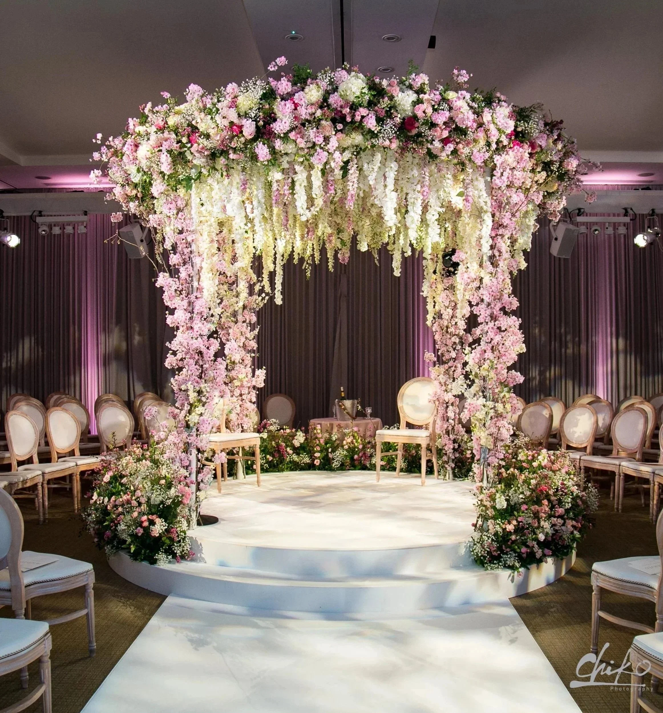 Elegant wedding ceremony setup with a floral arch and chairs arranged in a semi-circle on a white platform at Rosewood London