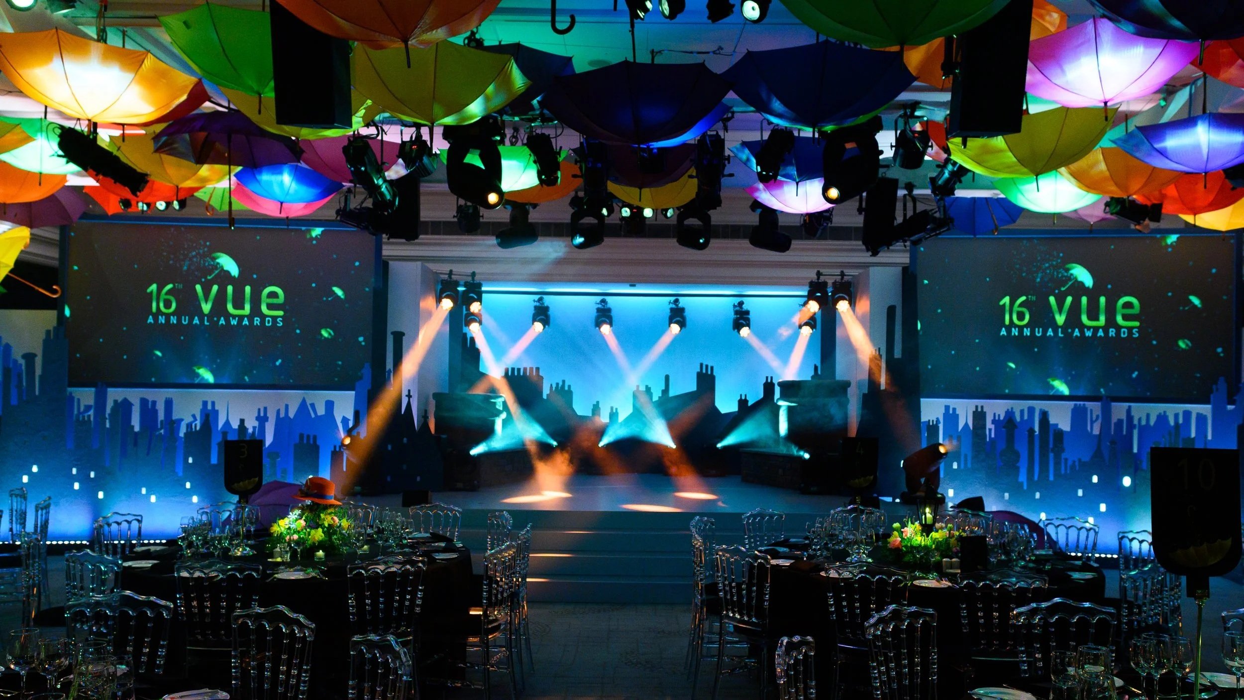 Indoor event space decorated with colorful umbrellas hanging from the ceiling, with stage lighting and large screens displaying the '16th VUE Annual Awards'.