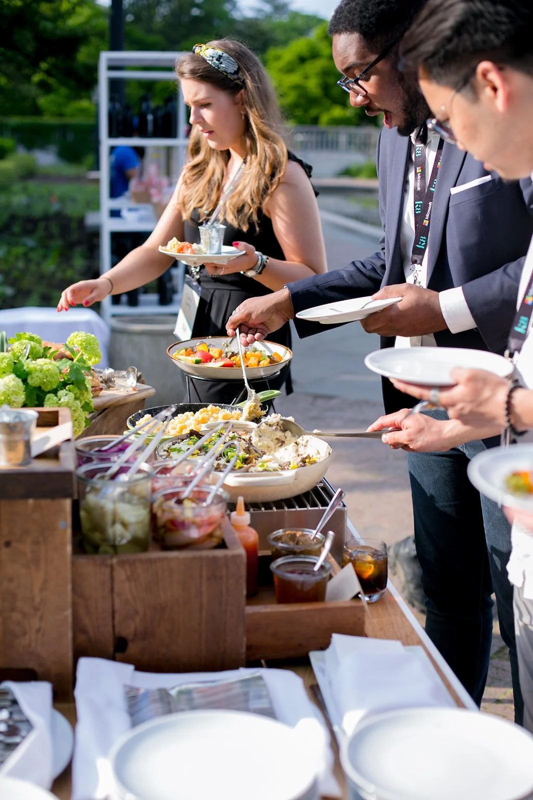 People serving themselves food at an outdoor buffet table.