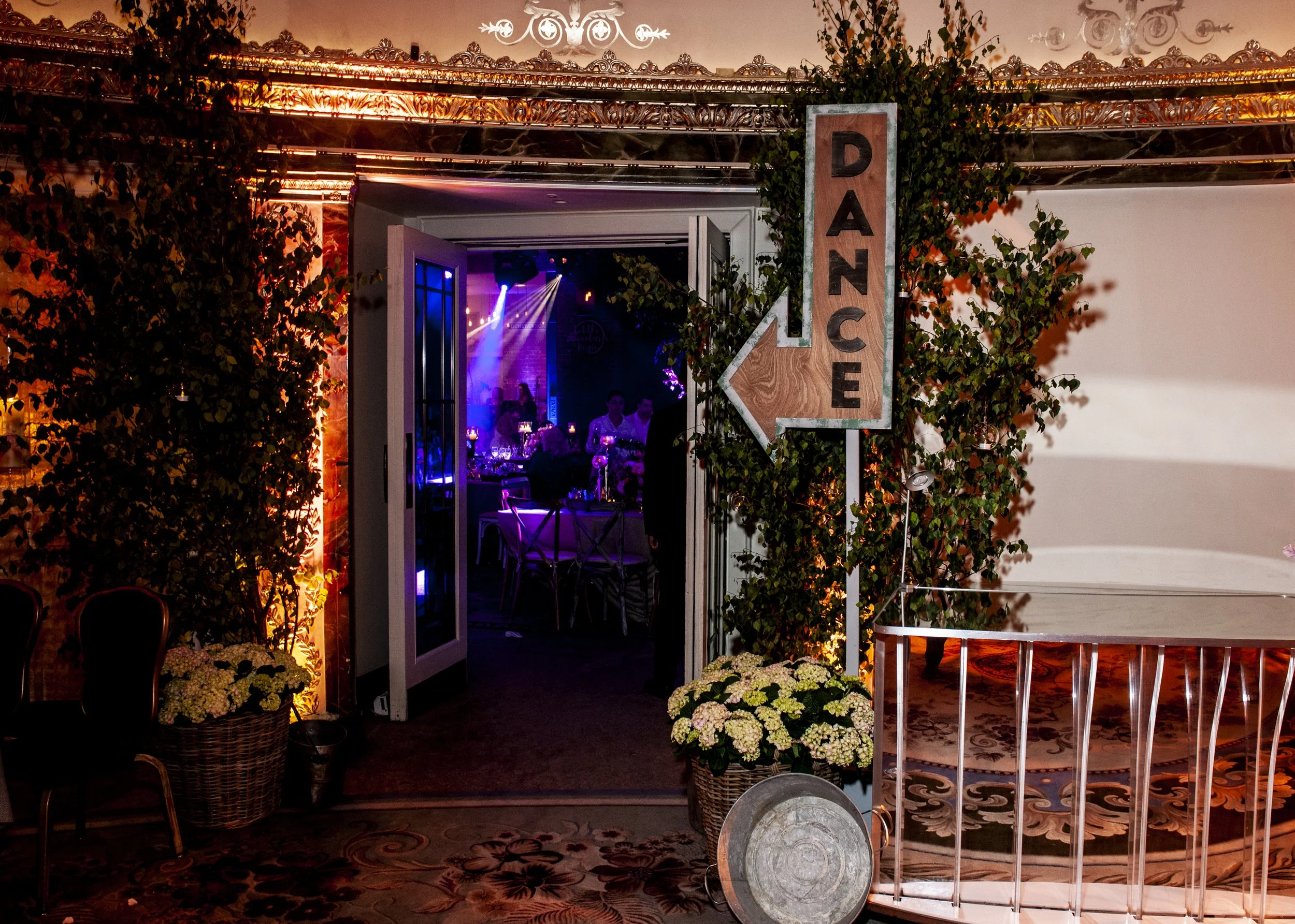 Entrance to a decorated event space with a welcome sign, floral arrangements, and colorful lighting.