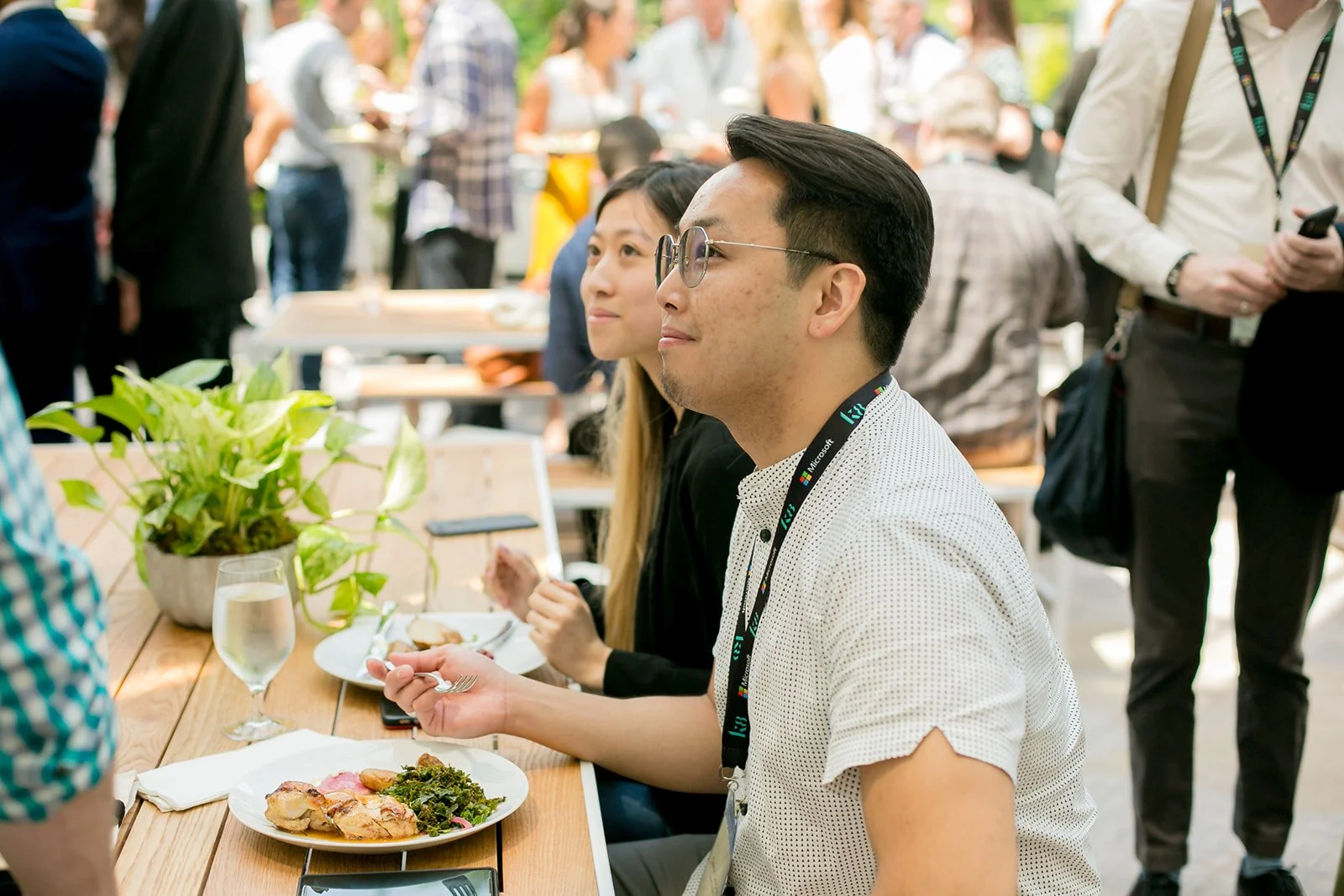 People sitting at a table during a conference or event, with food and drinks, and a man wearing glasses in the foreground.