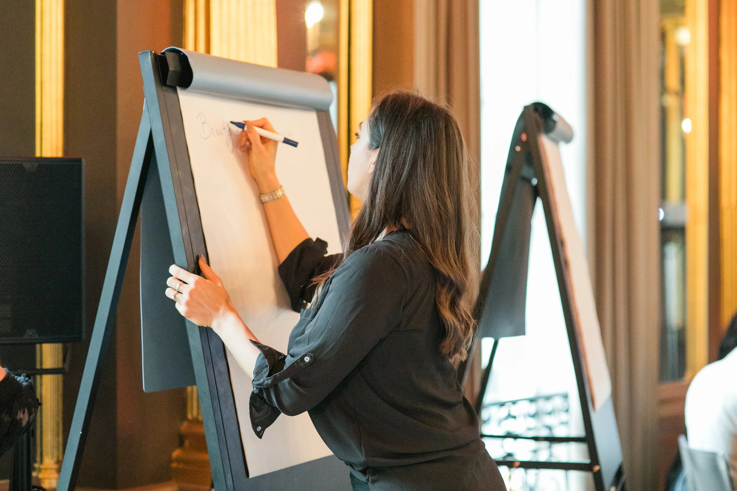 A woman writing on a large whiteboard with a marker in a conference or event room.
