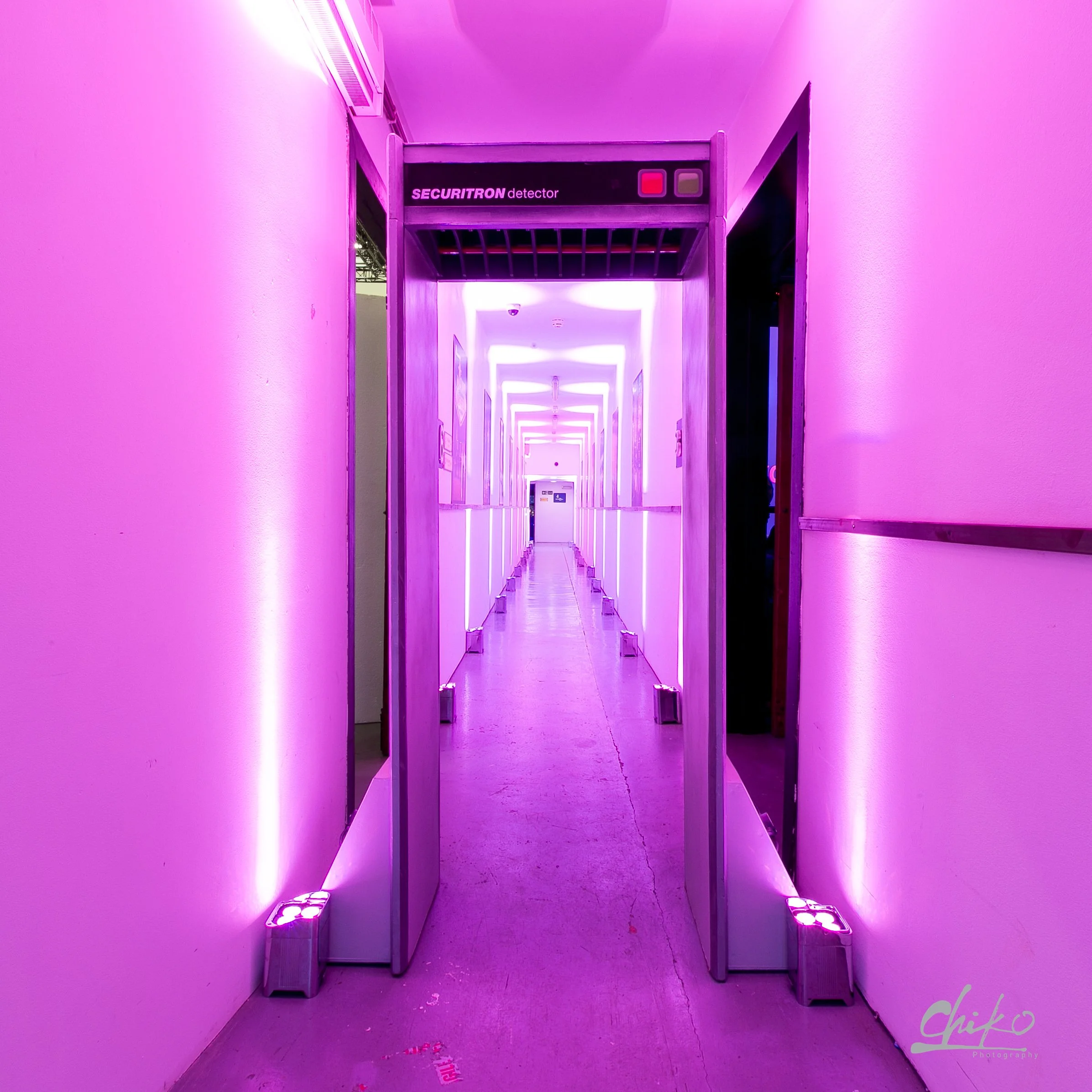 A hallway illuminated with purple and pink LED lighting, featuring security sensors labeled 'SECURITRON detector' at the doorway.