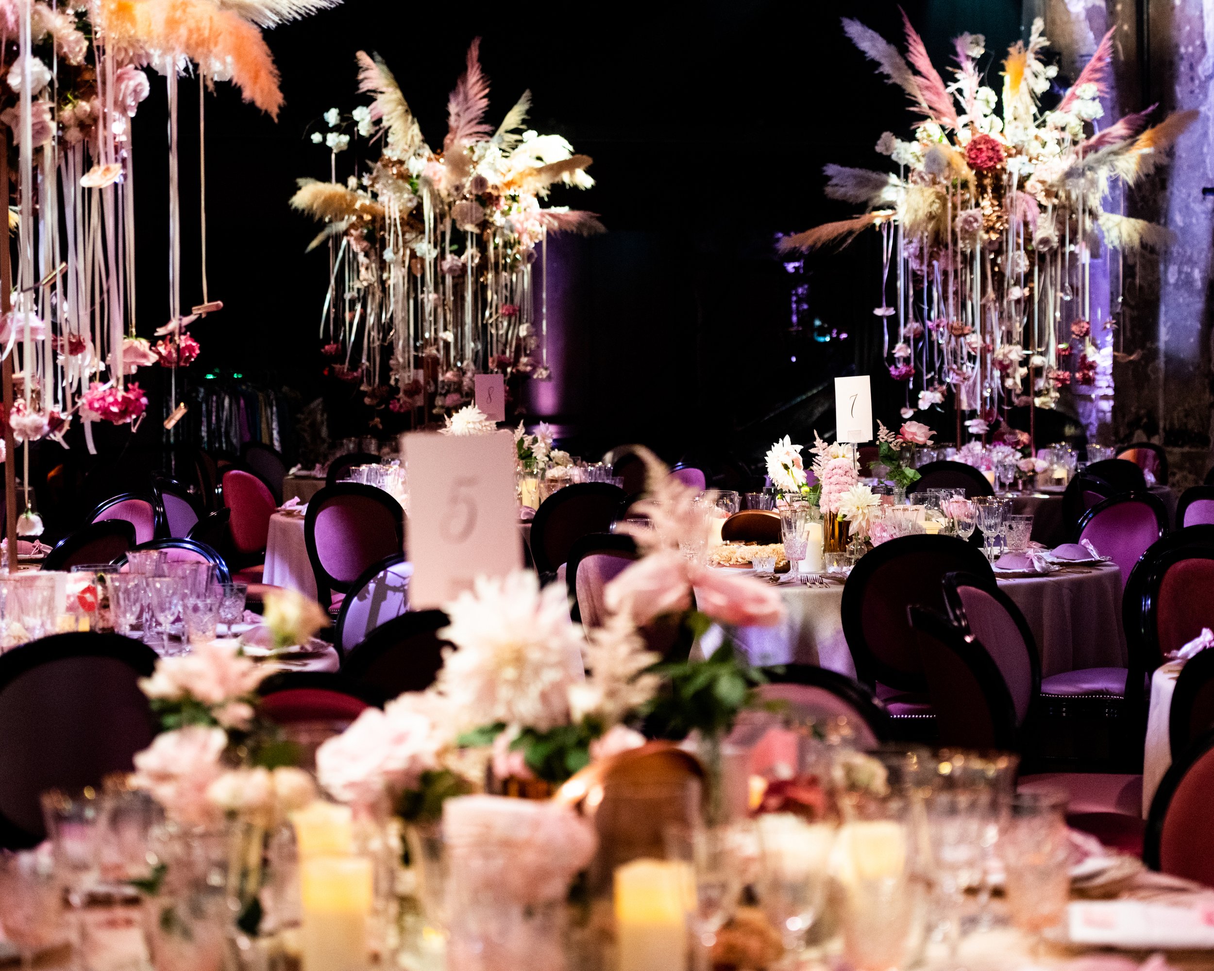 A banquet hall decorated with tall floral arrangements and curtains, set for a formal event with tables, glassware, and chairs. BAT MITZVAH AT BATTERSEA ARTS CENTRE