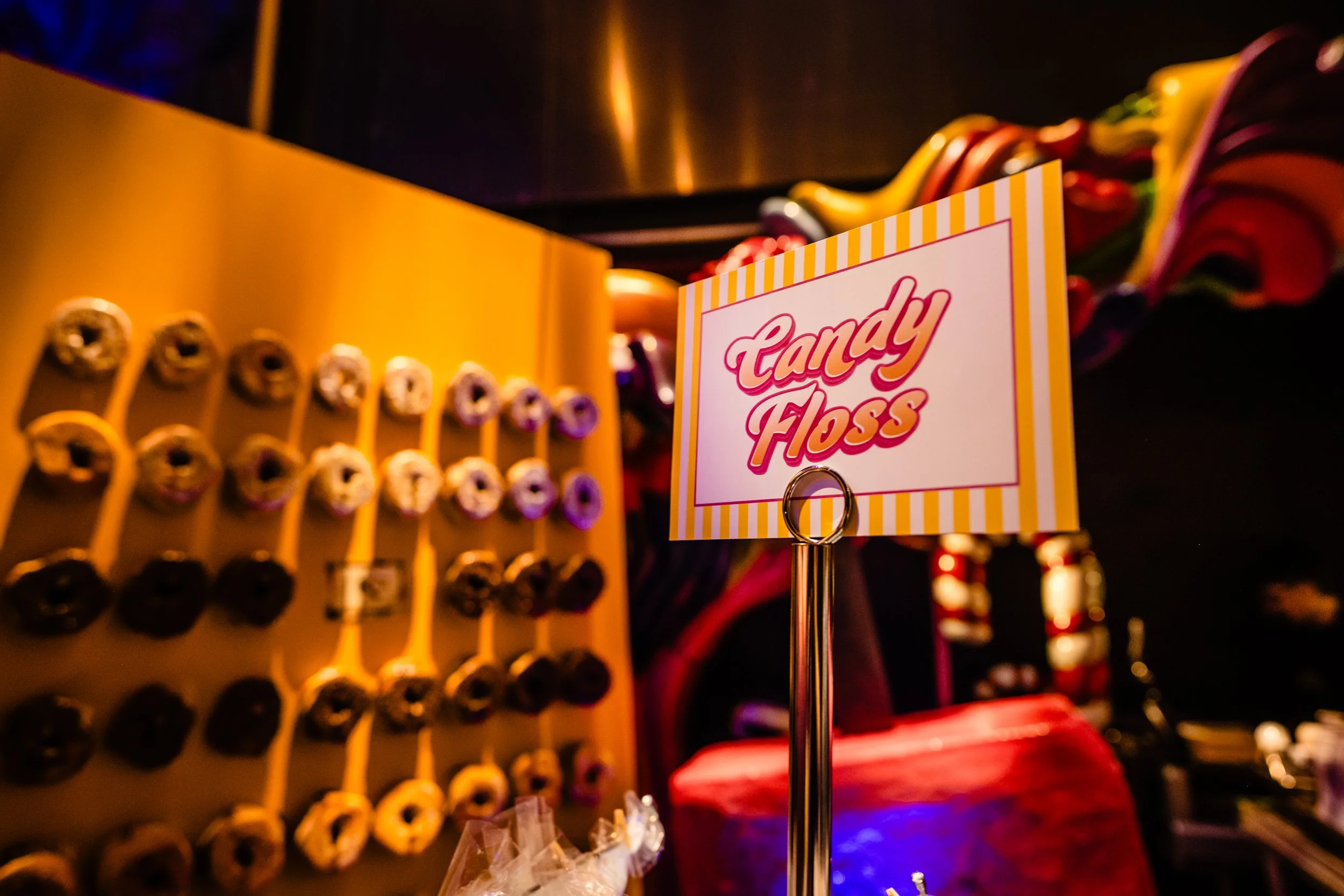 Close-up of a sign that says 'Candy Floss' next to a display of colorful candy floss in a store or fair setting.