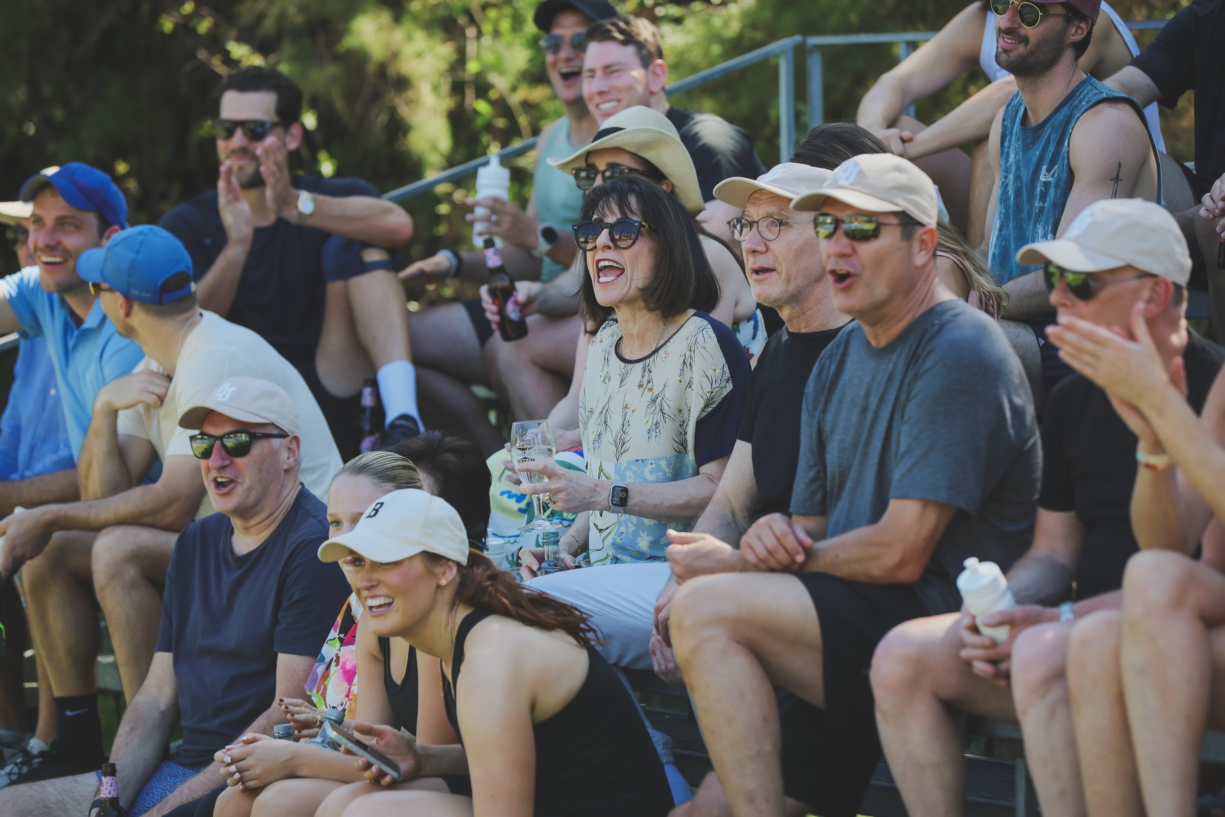 Group of people sitting on bleachers outdoors, enjoying a sunny day, some smiling, talking, and holding drinks at a Padel tournamanet at Anantara Villa Padierna Resort in Marbella