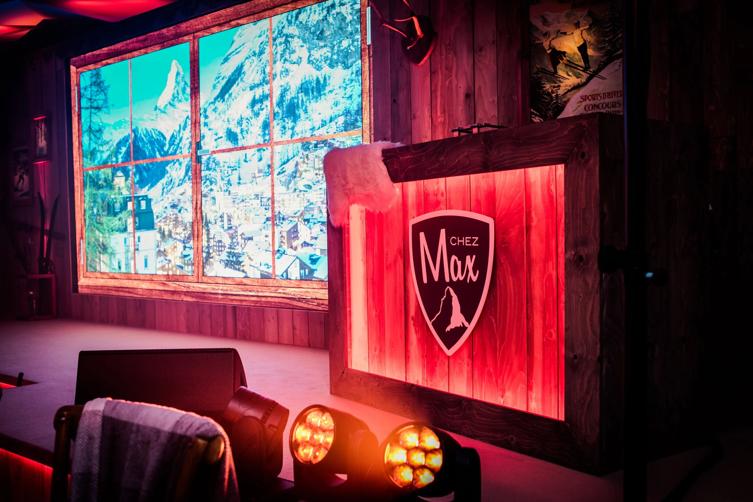 A stage with a wooden podium featuring a Mountaineers logo, in front a large window showing a snow-covered mountain landscape, adorned with a red fur cover on top, and red lighting illuminating the scene.