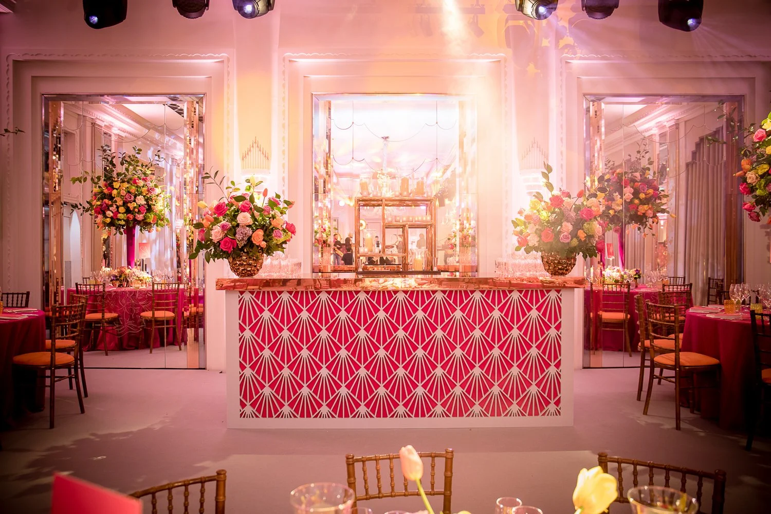Elegant event space with pink and gold decor, floral arrangements, and reflected lighting creating a glamorous atmosphere.