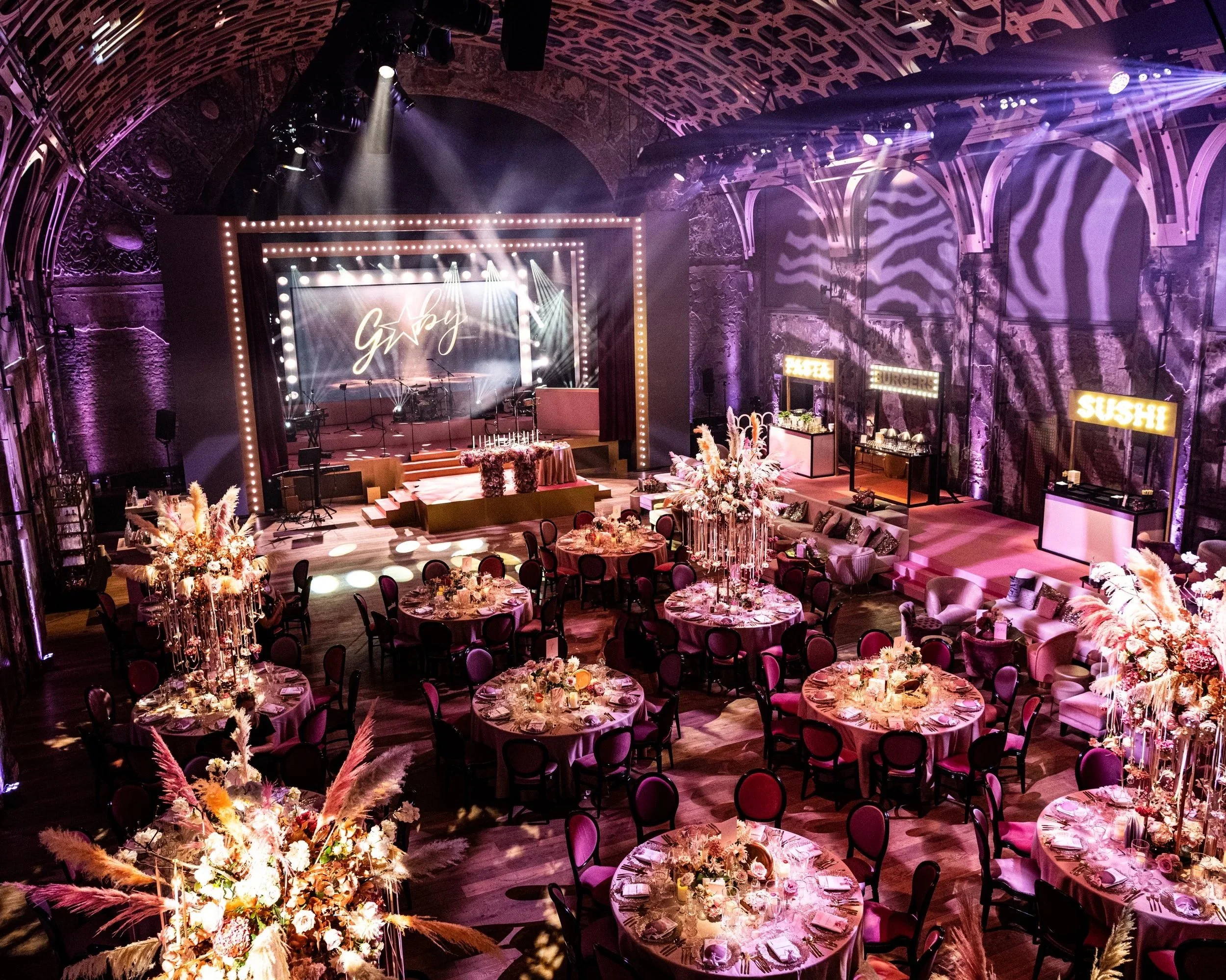 Hollywood Glamour celebration at Battersea Arts Centre, with pampas grass centrepieces, a lit stage sign and zebra-print projections across the stone walls