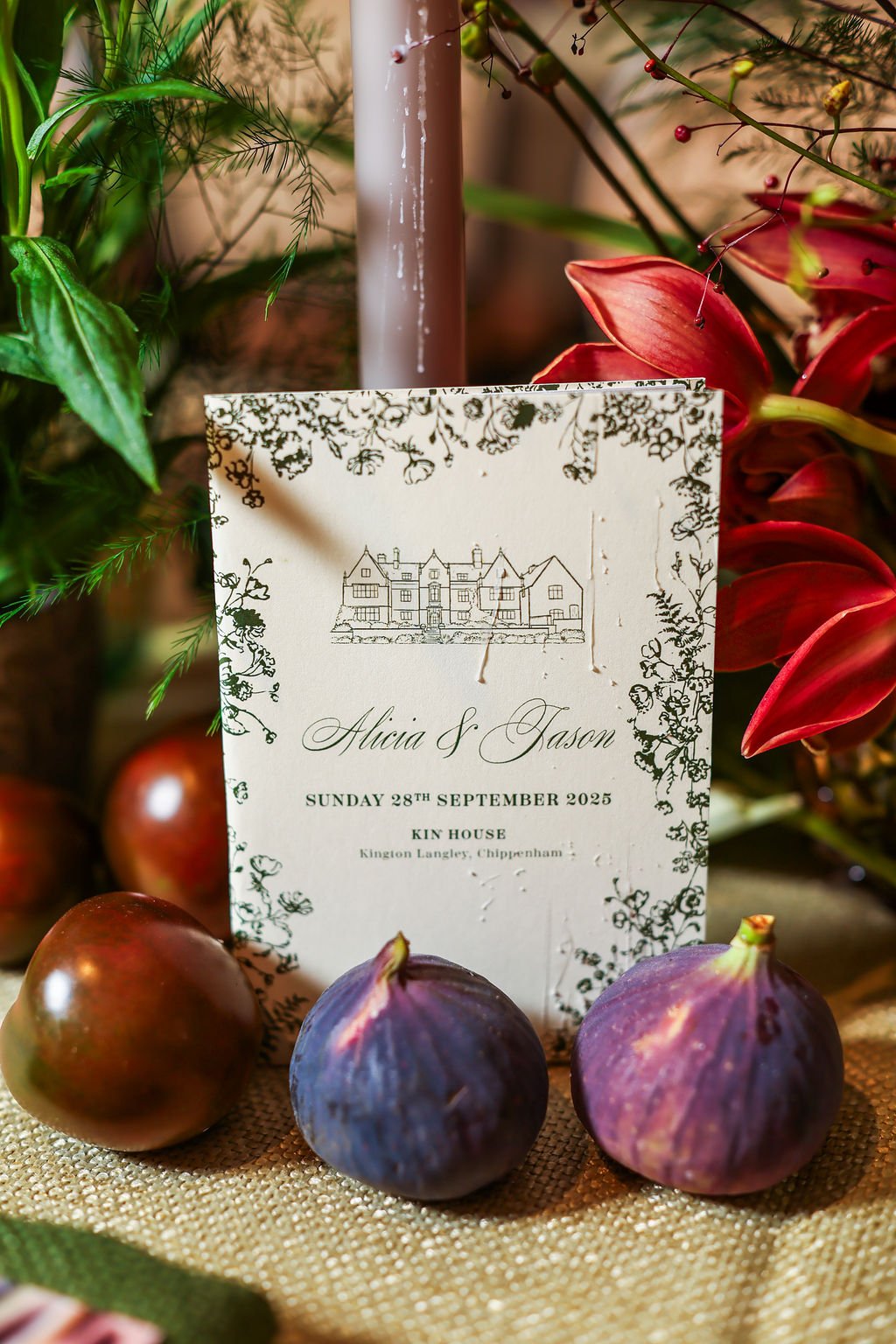 Wedding invitation placed among figs and red flowers, with greenery in the background.